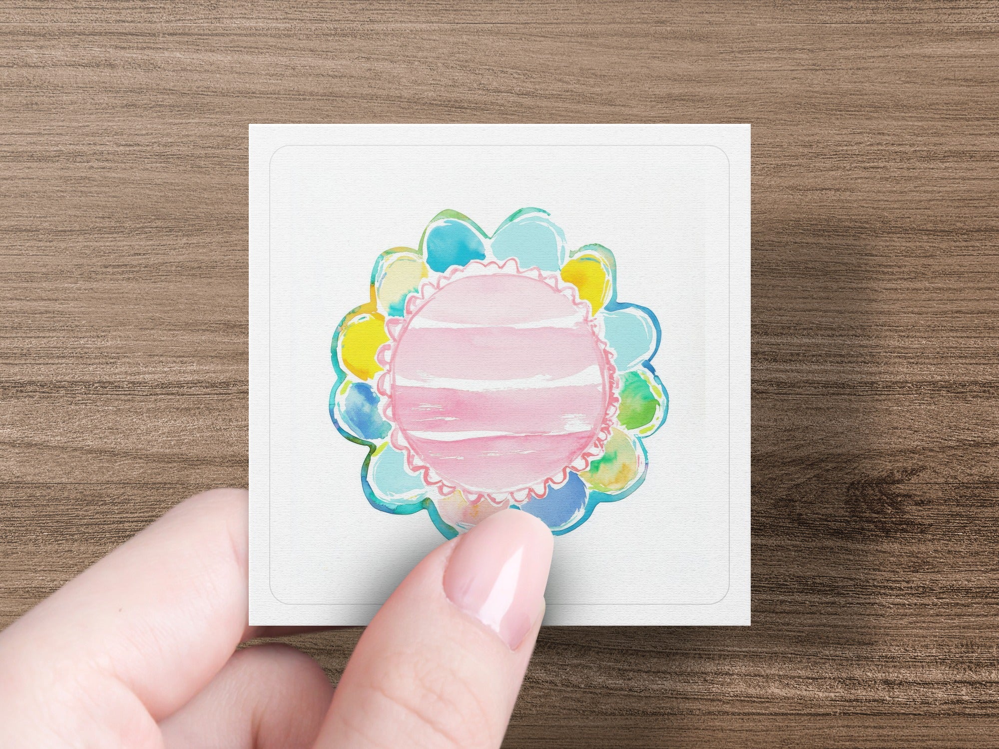 Hand holding square card with colorful floral watercolor design.