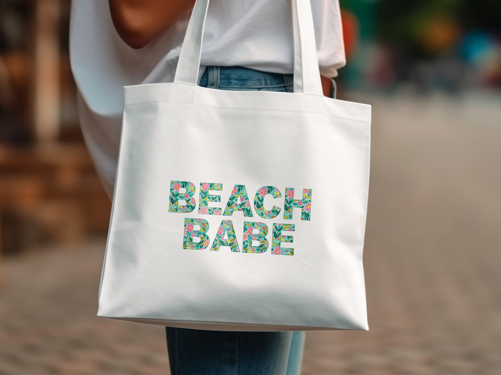White canvas tote bag with "BEACH BABE" text in floral pattern.
