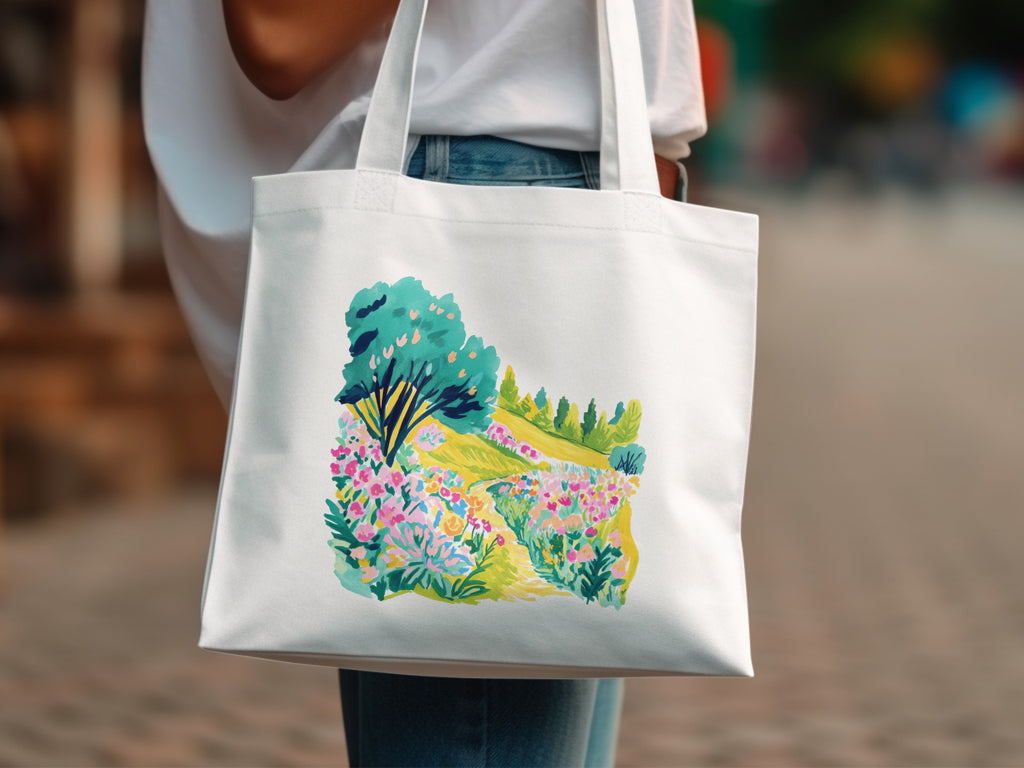 White tote bag with colorful floral landscape illustration.