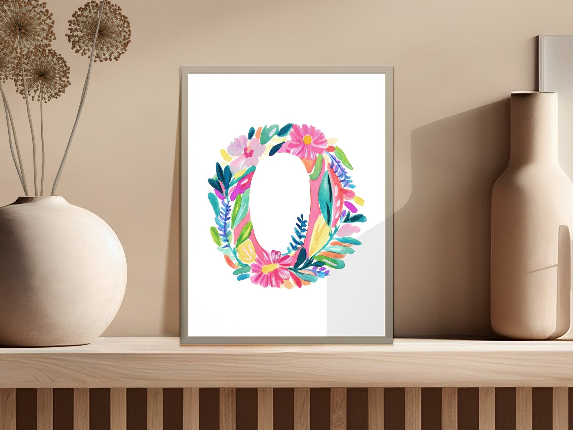 Colorful floral letter O artwork displayed in a white frame on a shelf.