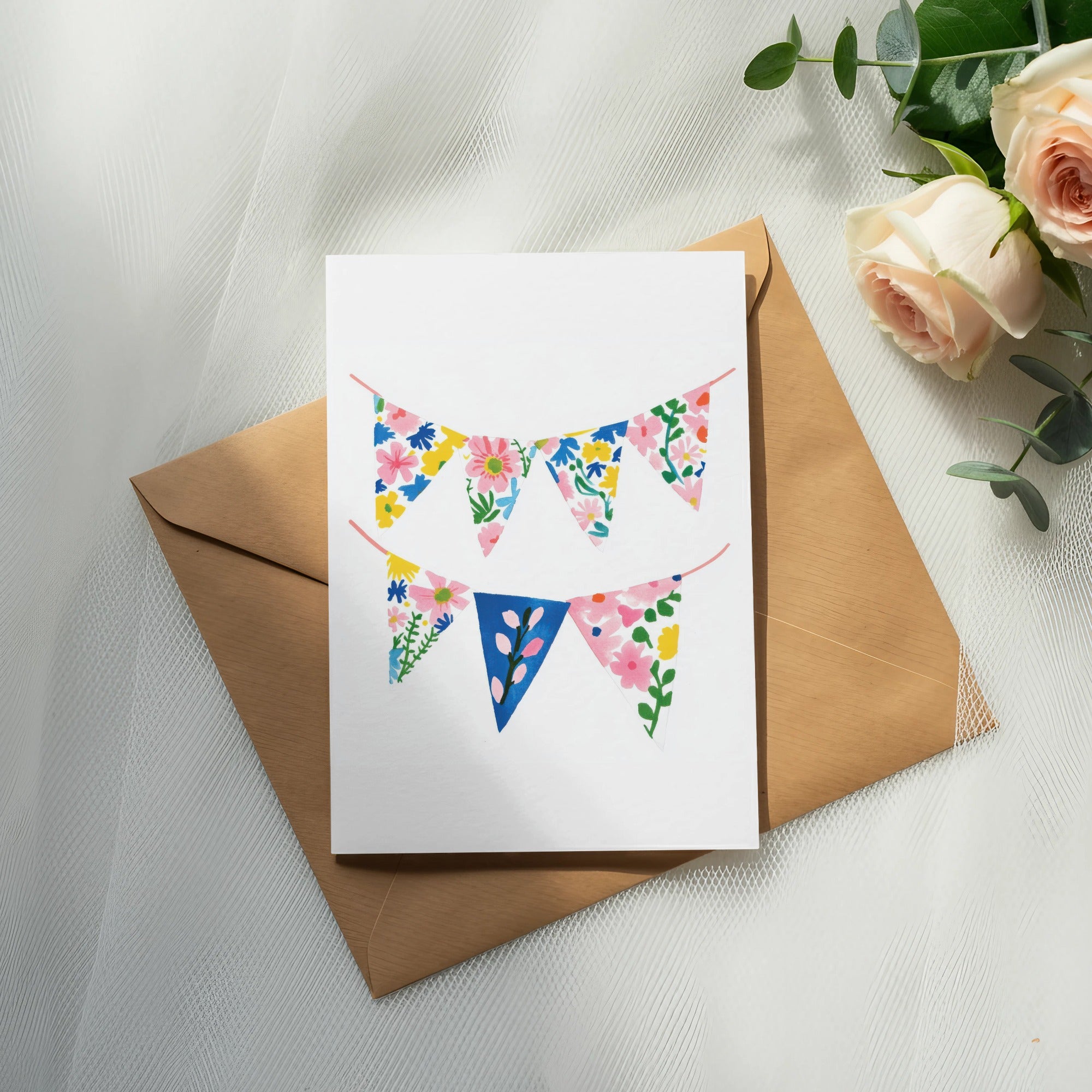Card with floral bunting, placed on a brown envelope and rose bouquet.