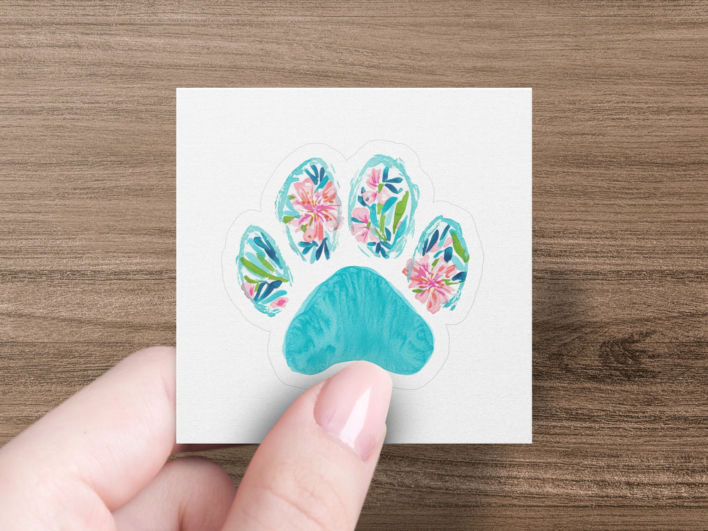 Turquoise paw print with floral watercolor design held by a hand.