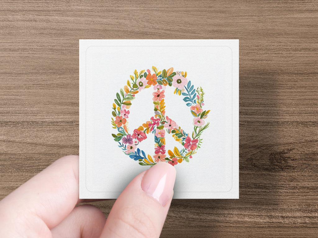 Floral peace sign wreath on square card held by a hand.