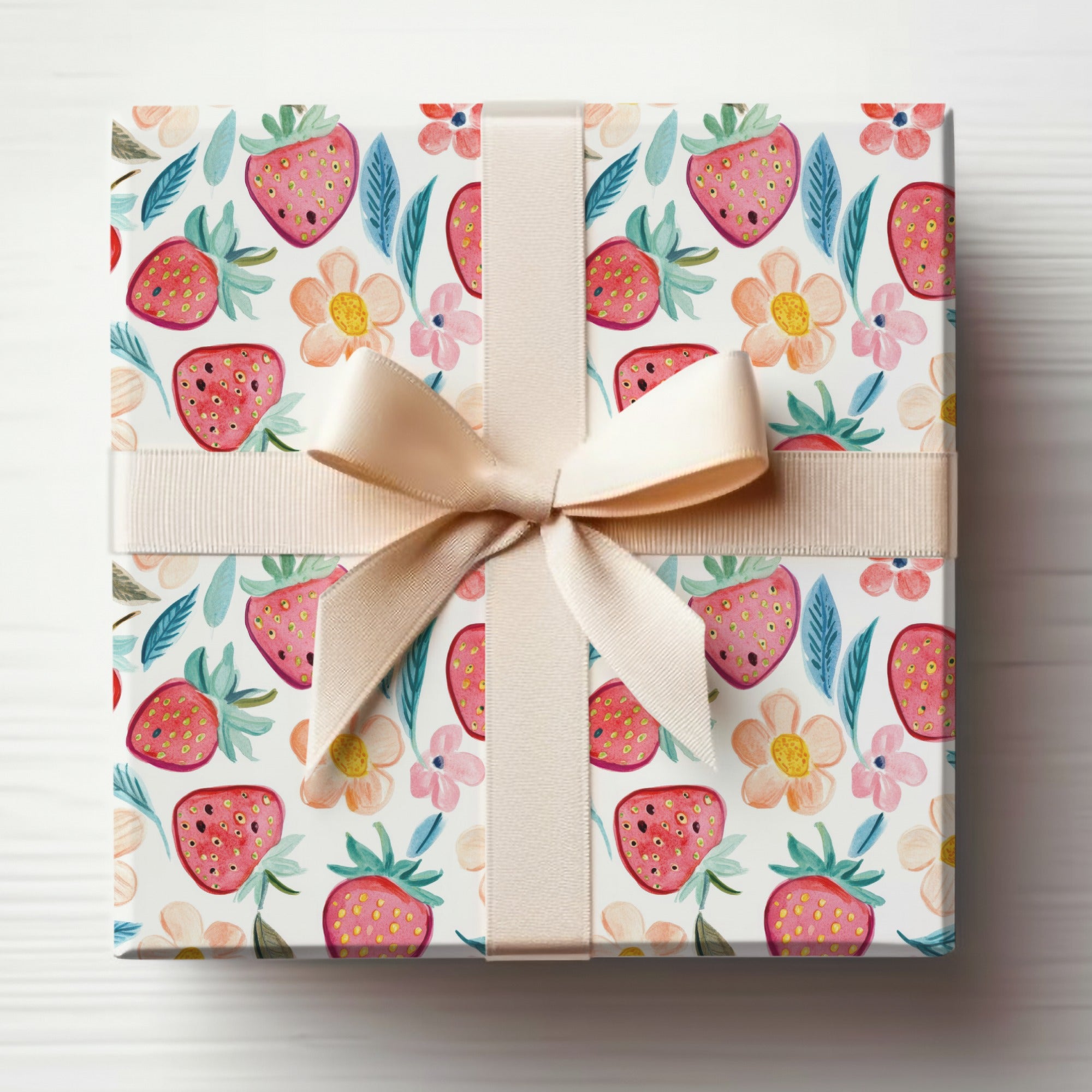 Gift box with strawberry and floral pattern, tied with a light brown ribbon.