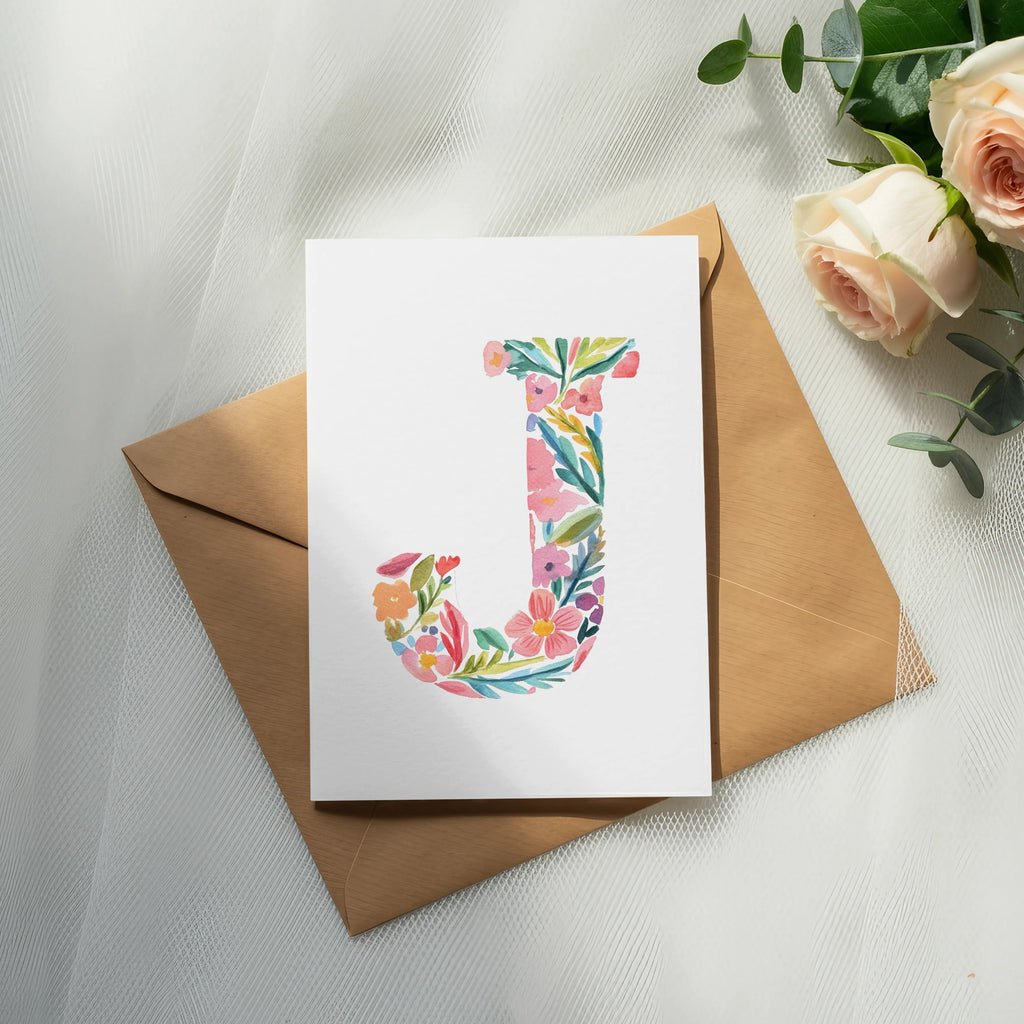 Card with floral letter "J" on a brown envelope with roses and eucalyptus.