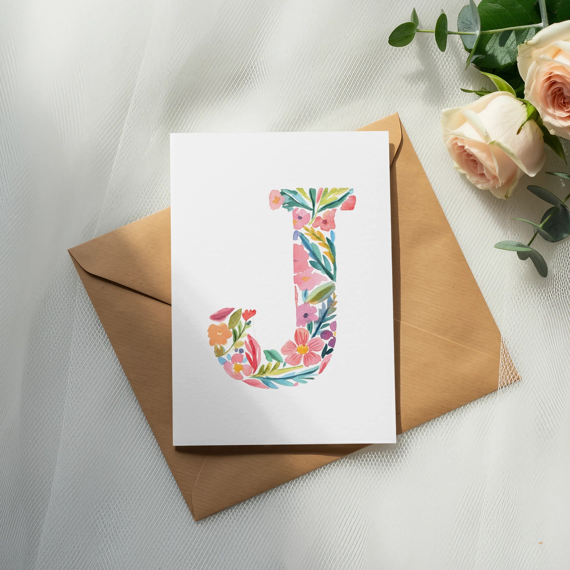 Card with floral letter "J" on a brown envelope with roses and eucalyptus.