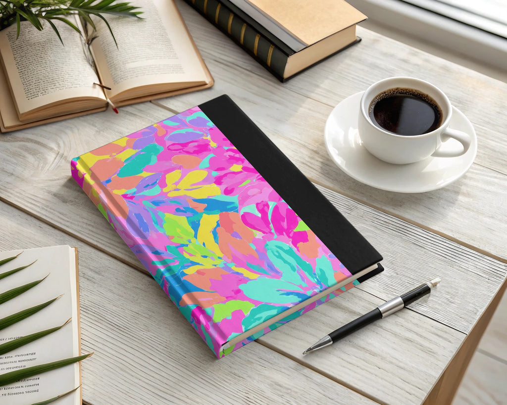 Colorful floral notebook with pen and coffee cup on a desk.