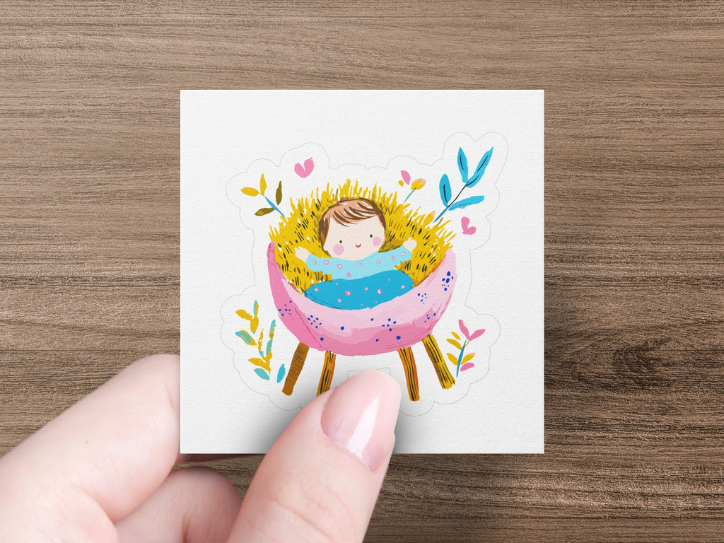 Baby Jesus sleeping in a pink manger with yellow and blue floral accents.