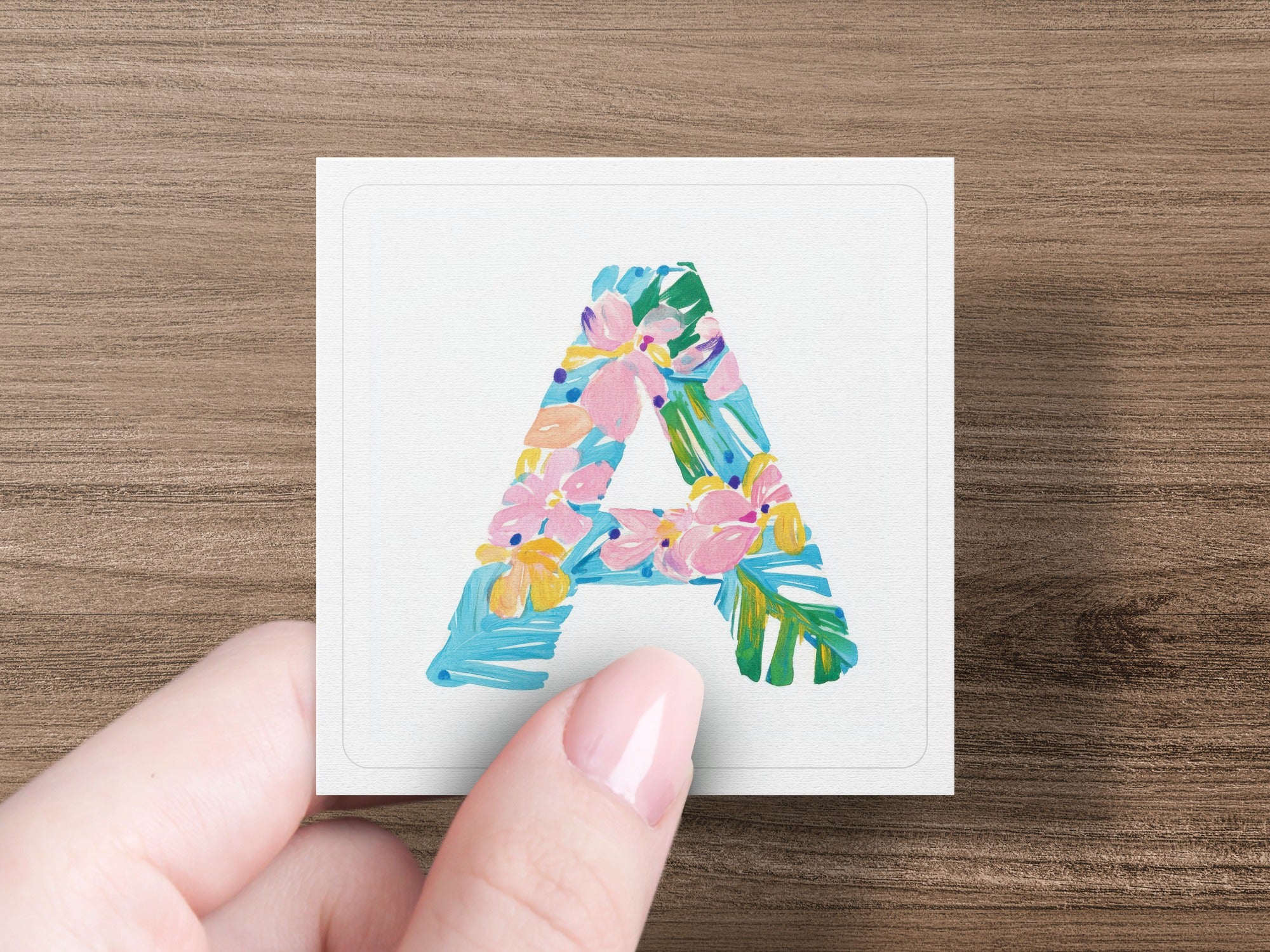 Letter A with floral pattern held by fingers.