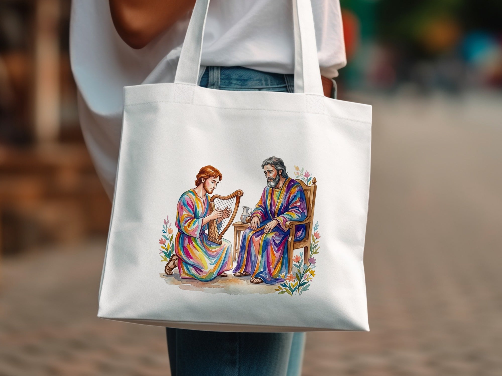 Woman in white shirt holds tote bag with watercolor painting of David playing harp for King Saul.