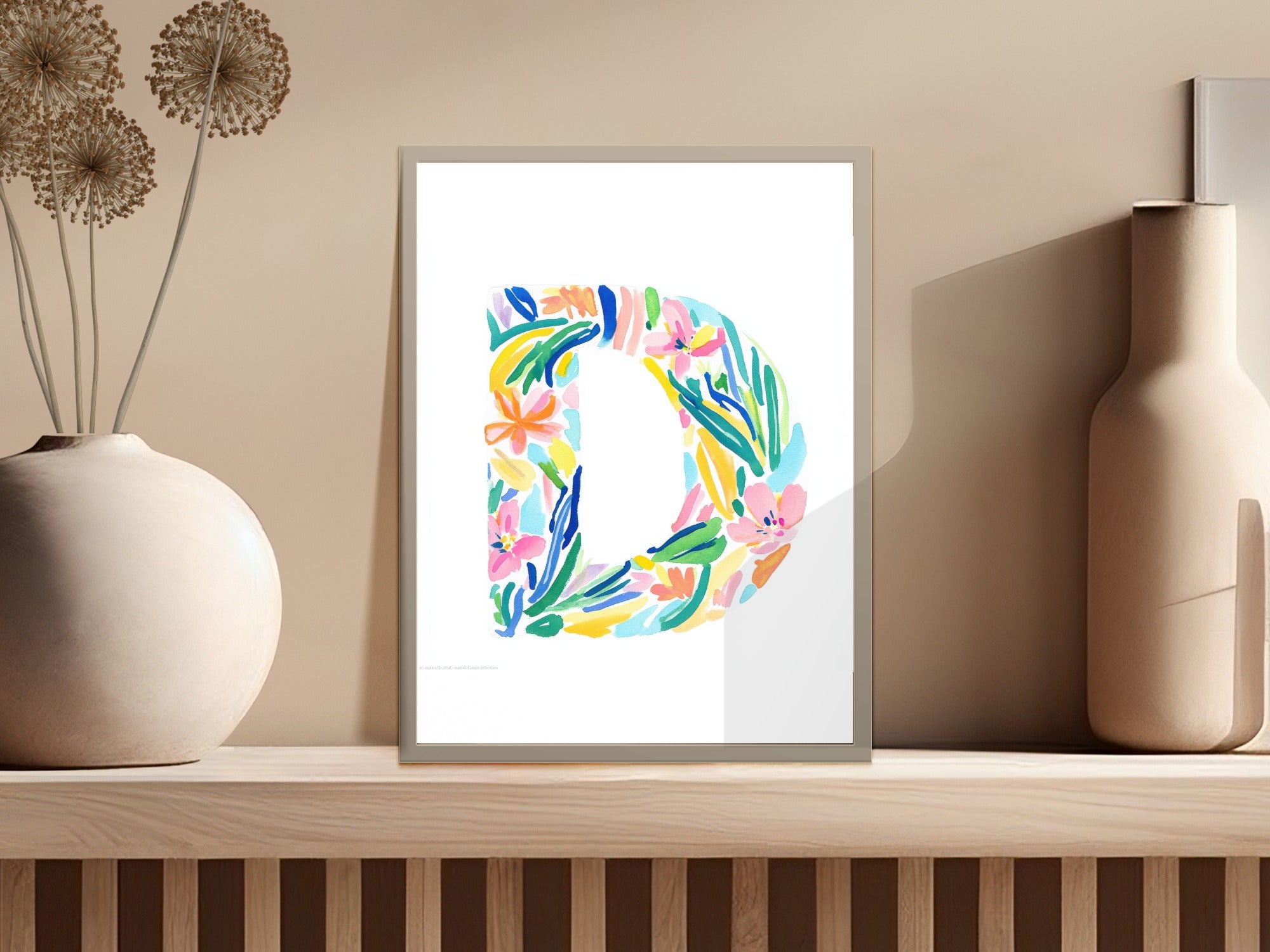 Colorful floral letter D print in a frame on a shelf.