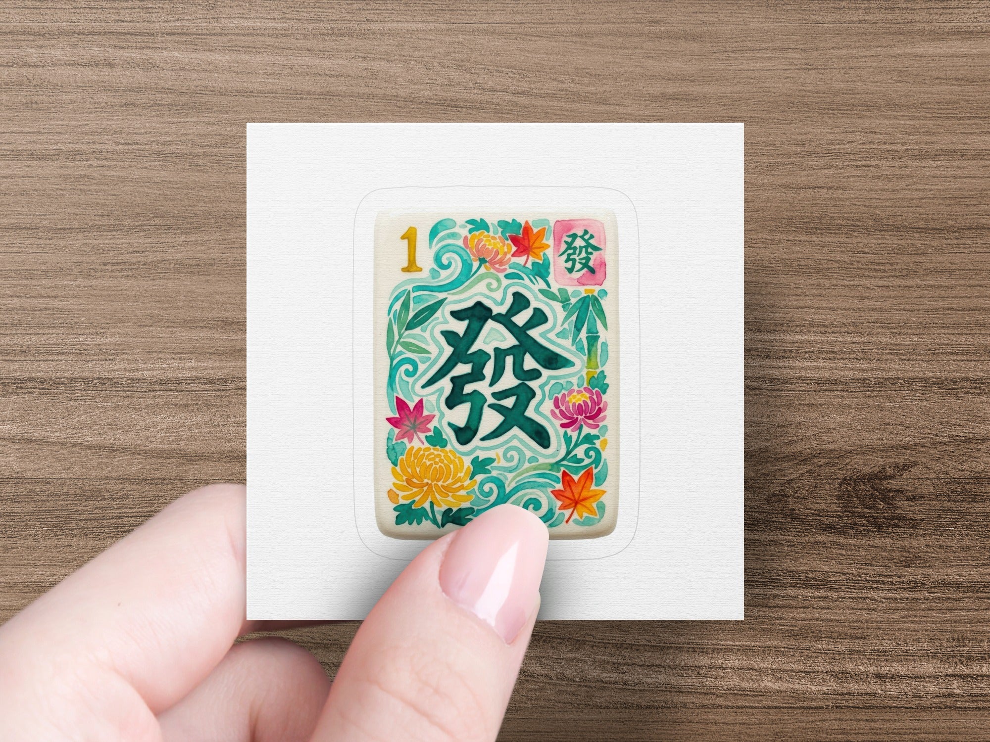Mahjong tile with Chinese characters and floral designs, held by a hand.