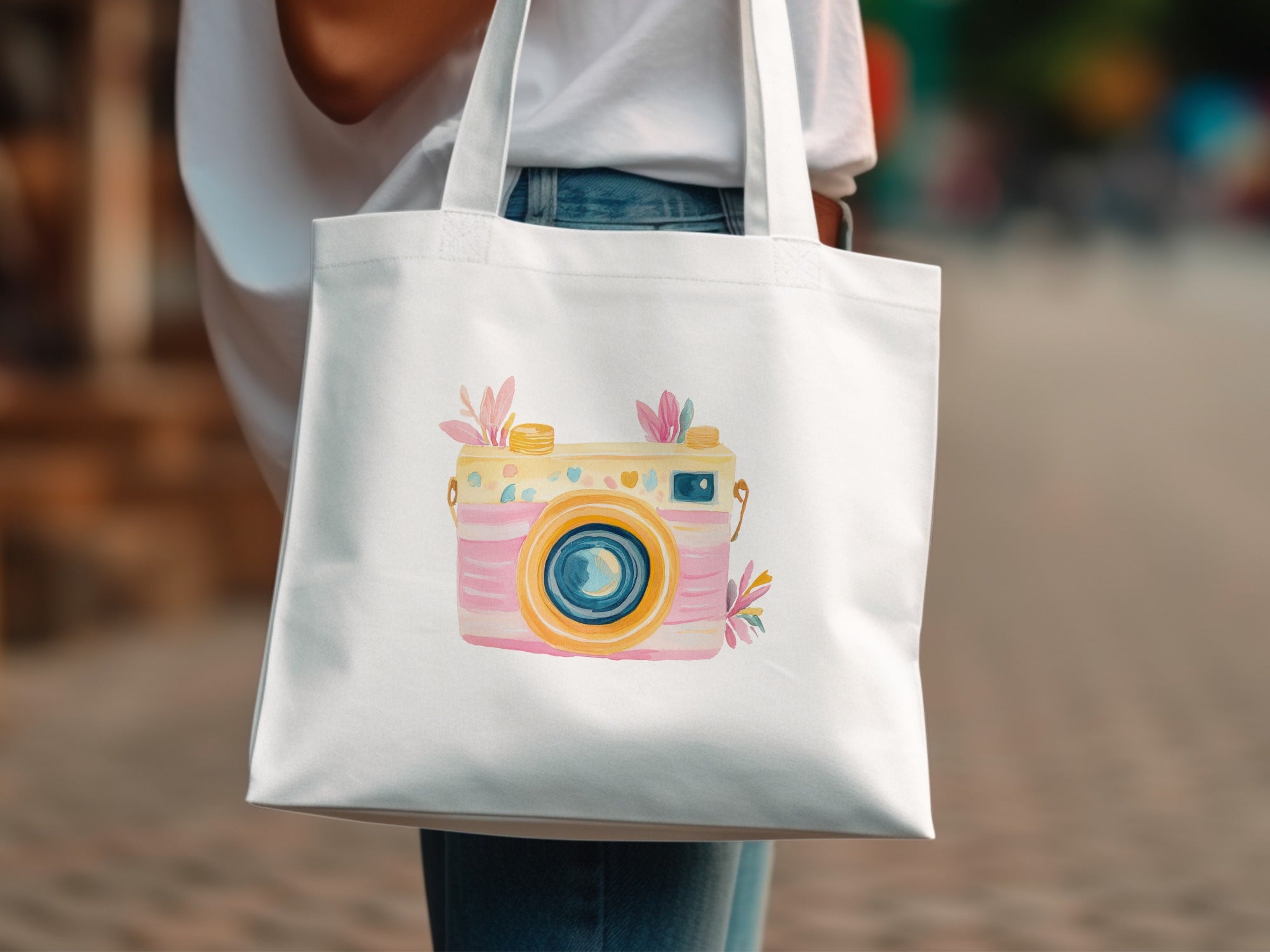 White tote bag with a watercolor illustration of a pink and yellow camera.