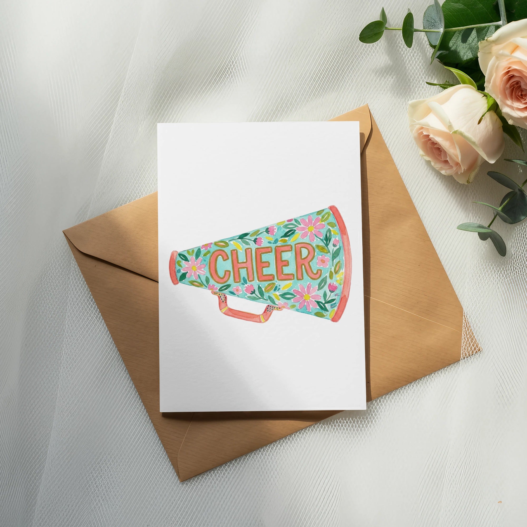 Watercolor "CHEER" megaphone with floral accents on a card, placed on an envelope.