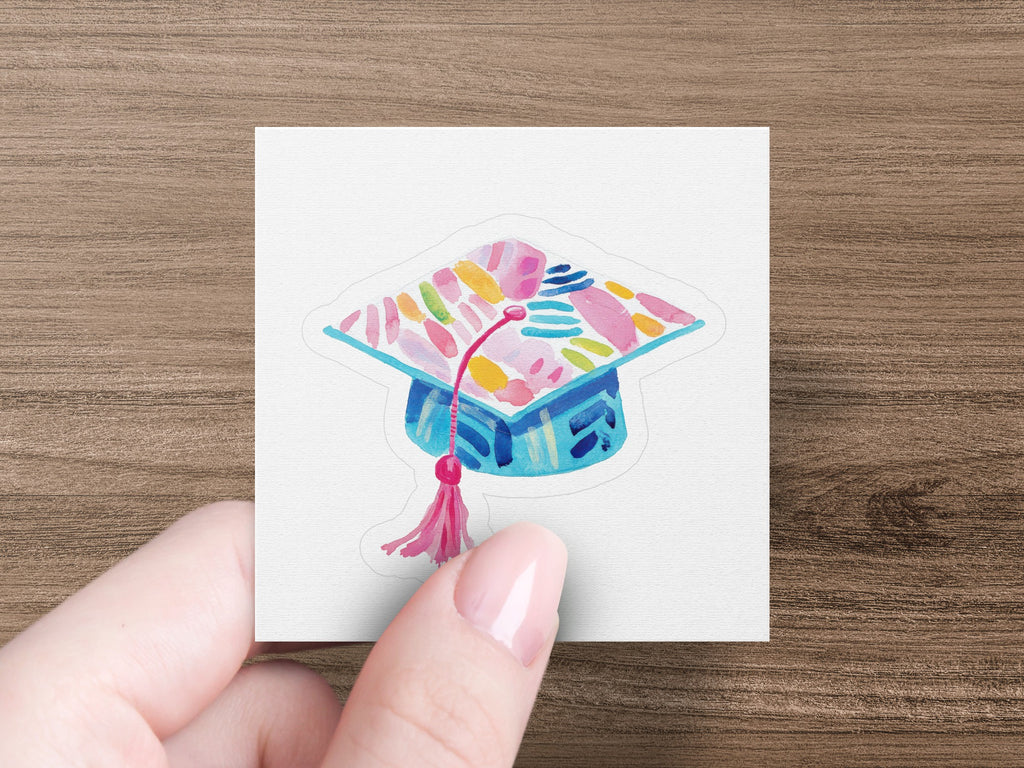Blue graduation cap with colorful abstract pattern and pink tassel.