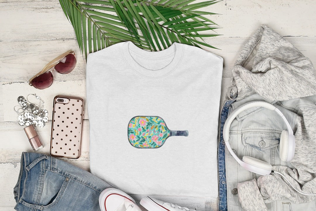 White t-shirt with a colorful floral pickleball paddle graphic.
