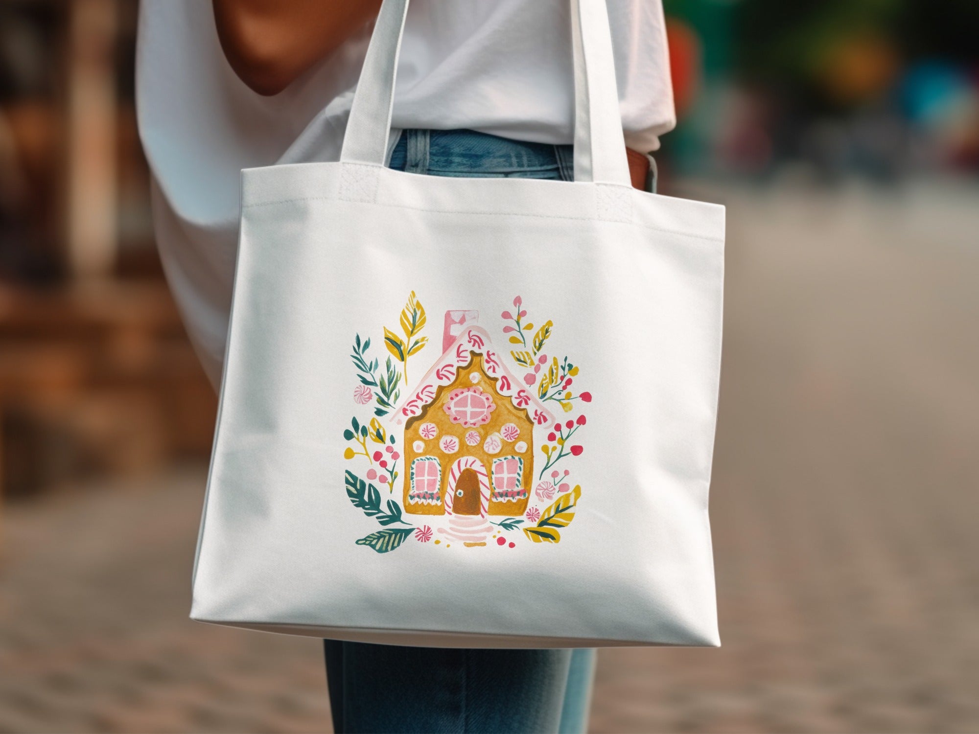 White tote bag with a watercolor gingerbread house illustration and floral accents.