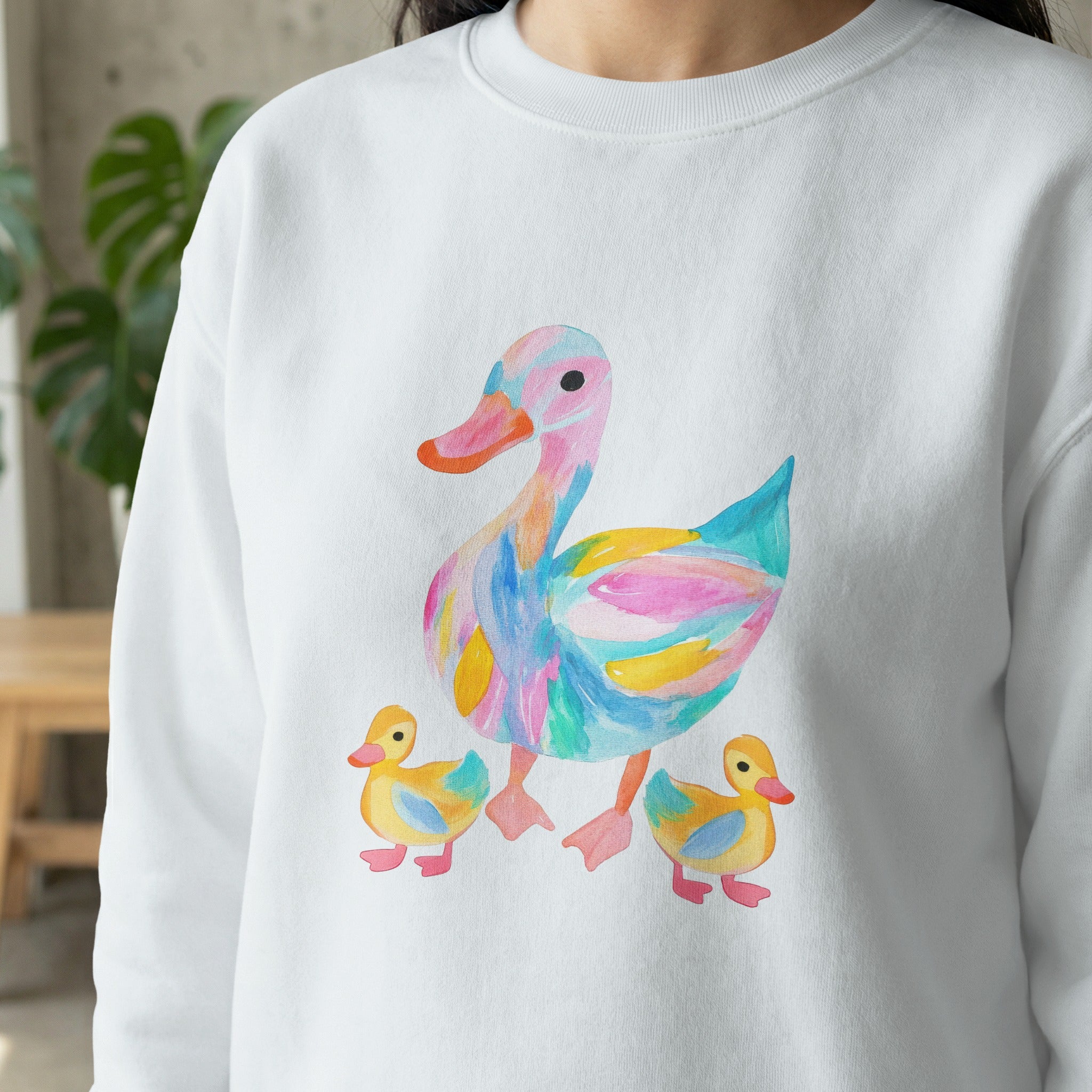 Watercolor duck family with colorful abstract patterns on a white sweatshirt.