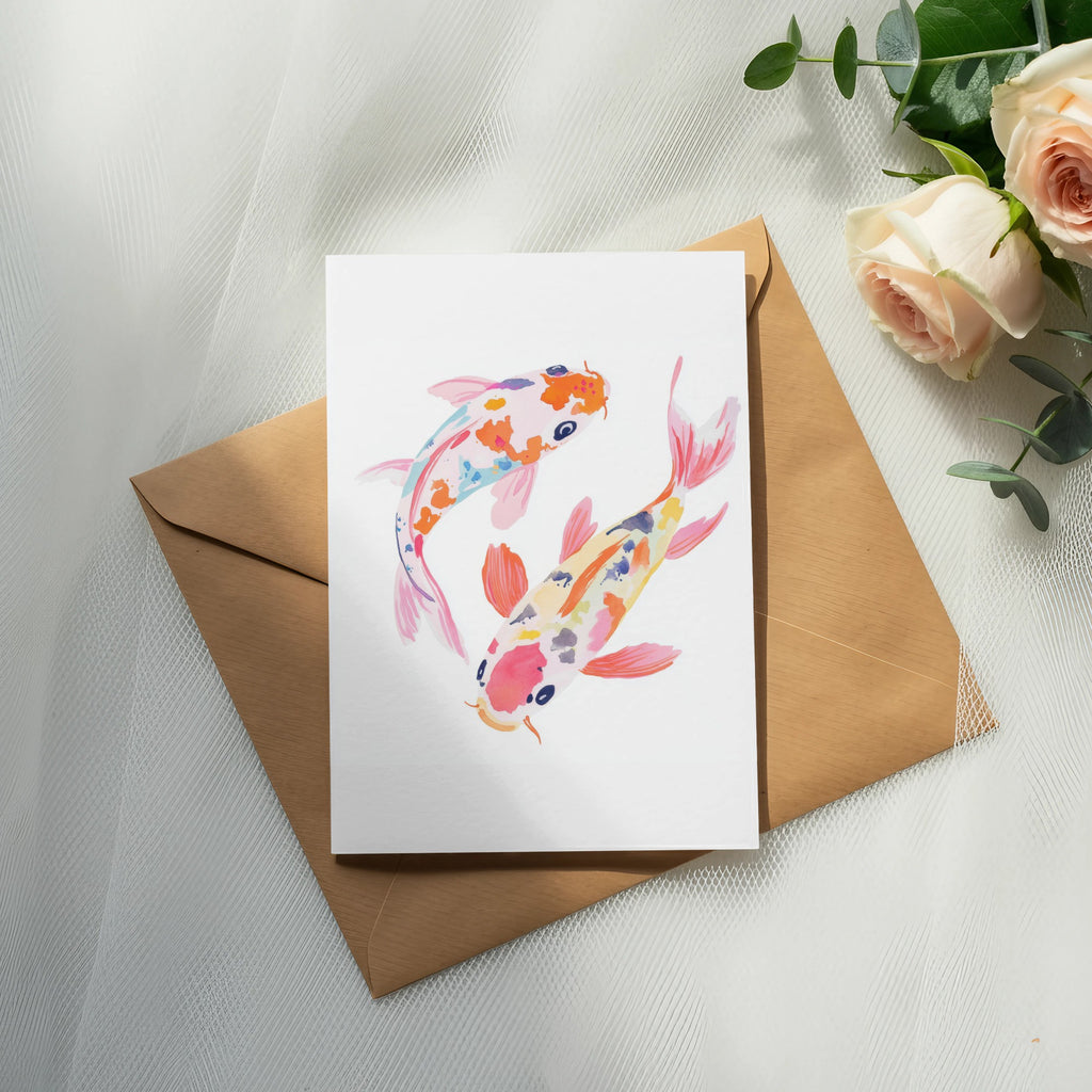 Two colorful koi fish watercolor painting on a card, resting on an envelope with roses.