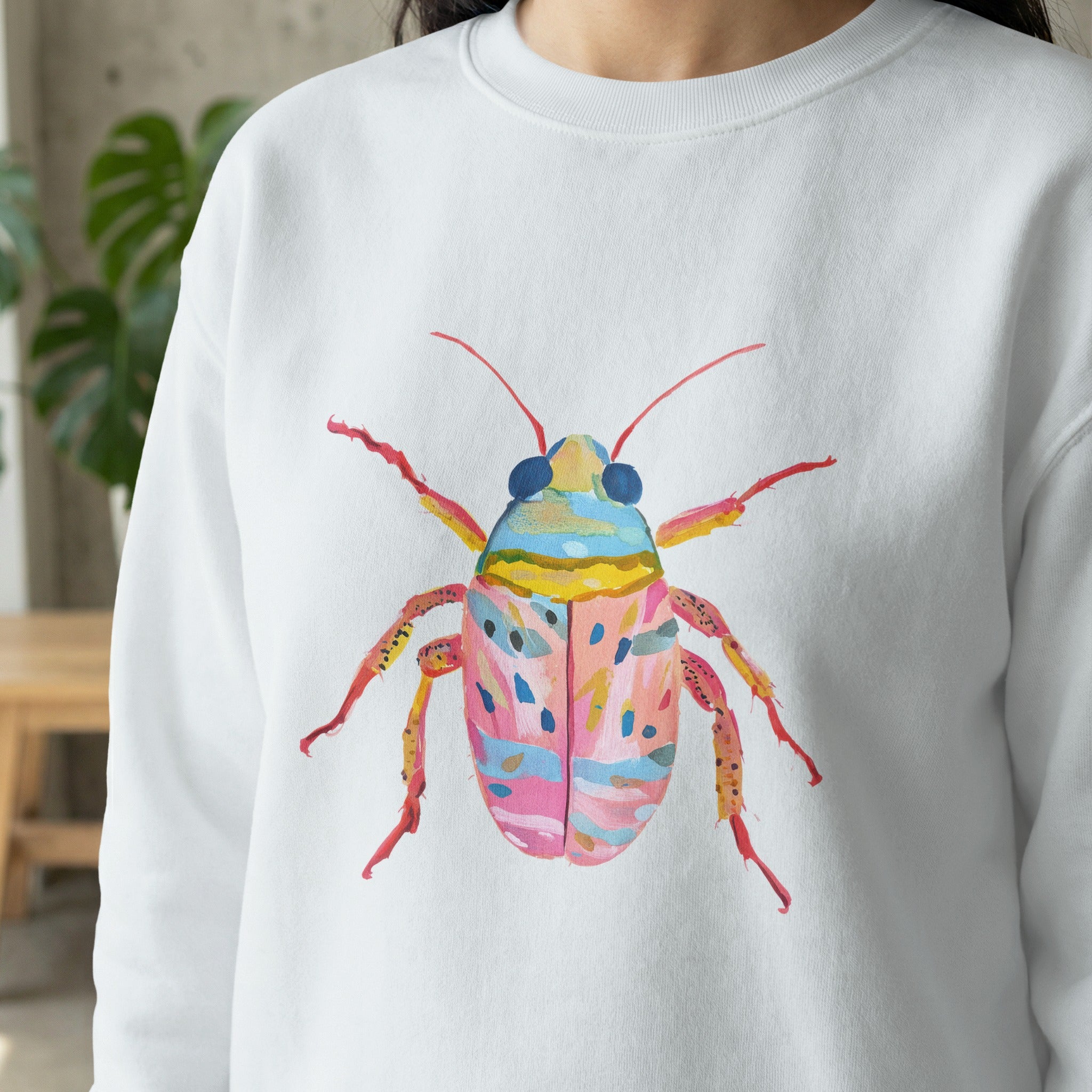 Watercolor illustration of a colorful bug on a white sweatshirt.