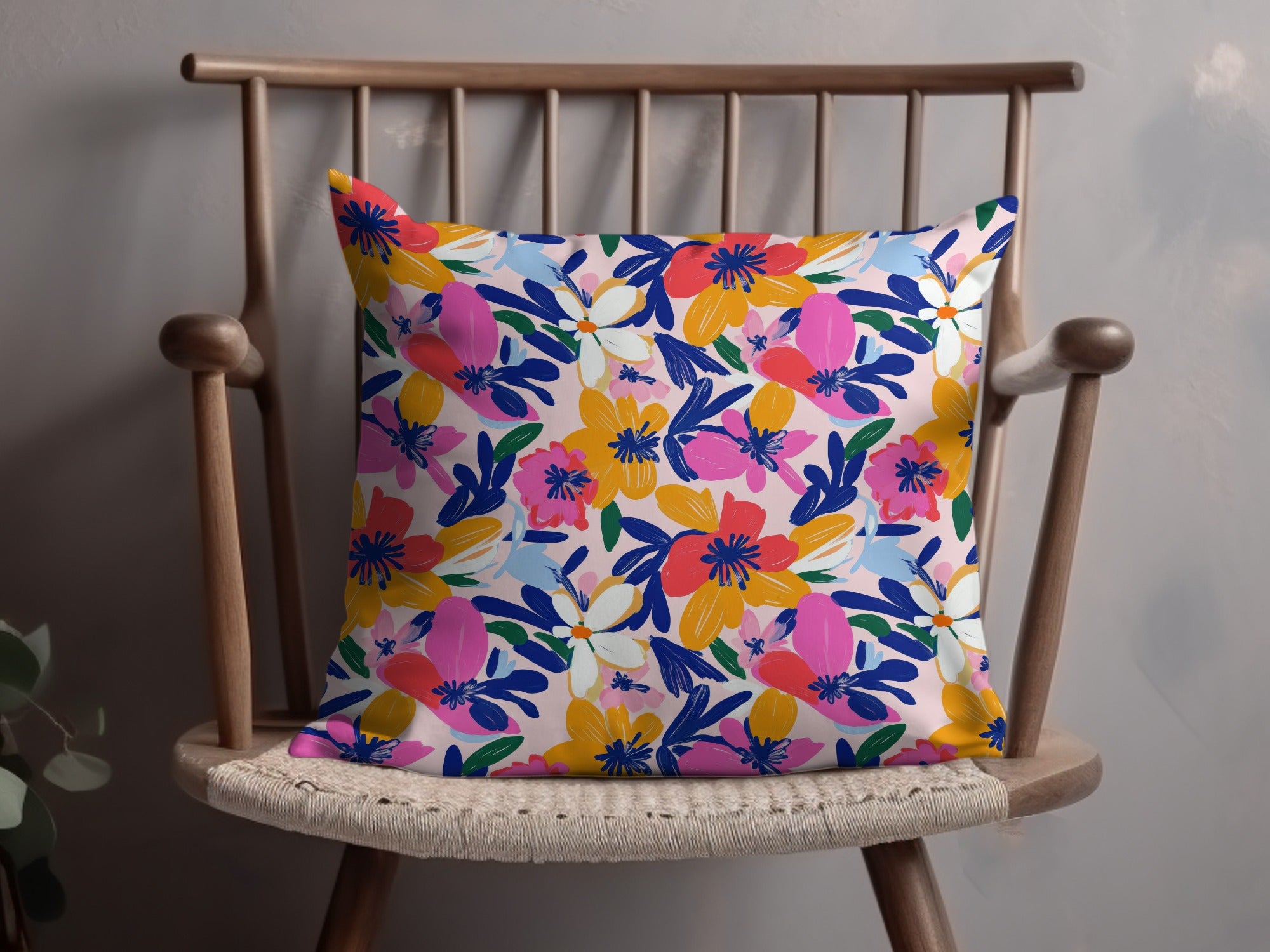 Floral print pillow with pink, blue, yellow, and white flowers on a light pink background.