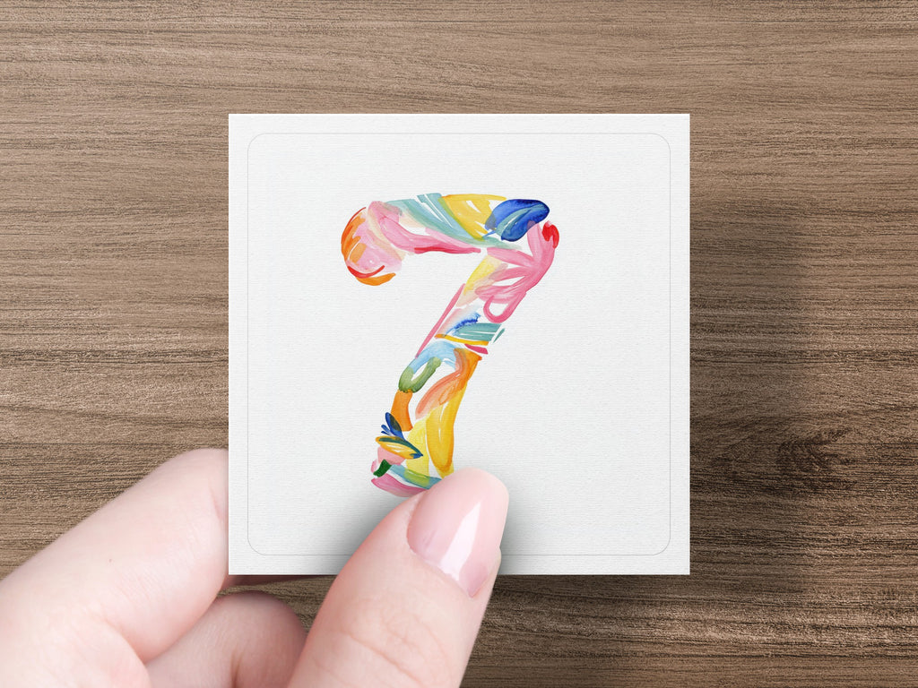 A hand holds a square card with a colorful, abstract number seven.