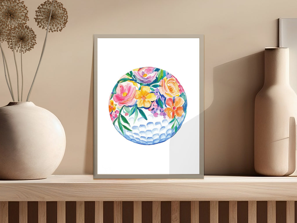Watercolor floral golf ball art in a framed print on a shelf.