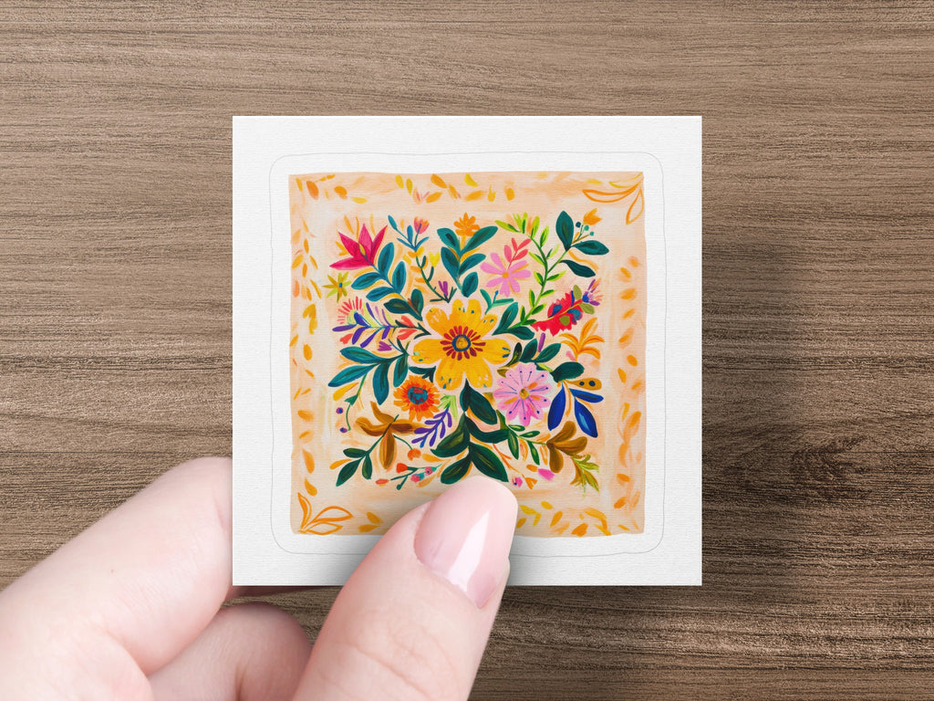 Hand holding square sticker with colorful folk art floral bouquet design.