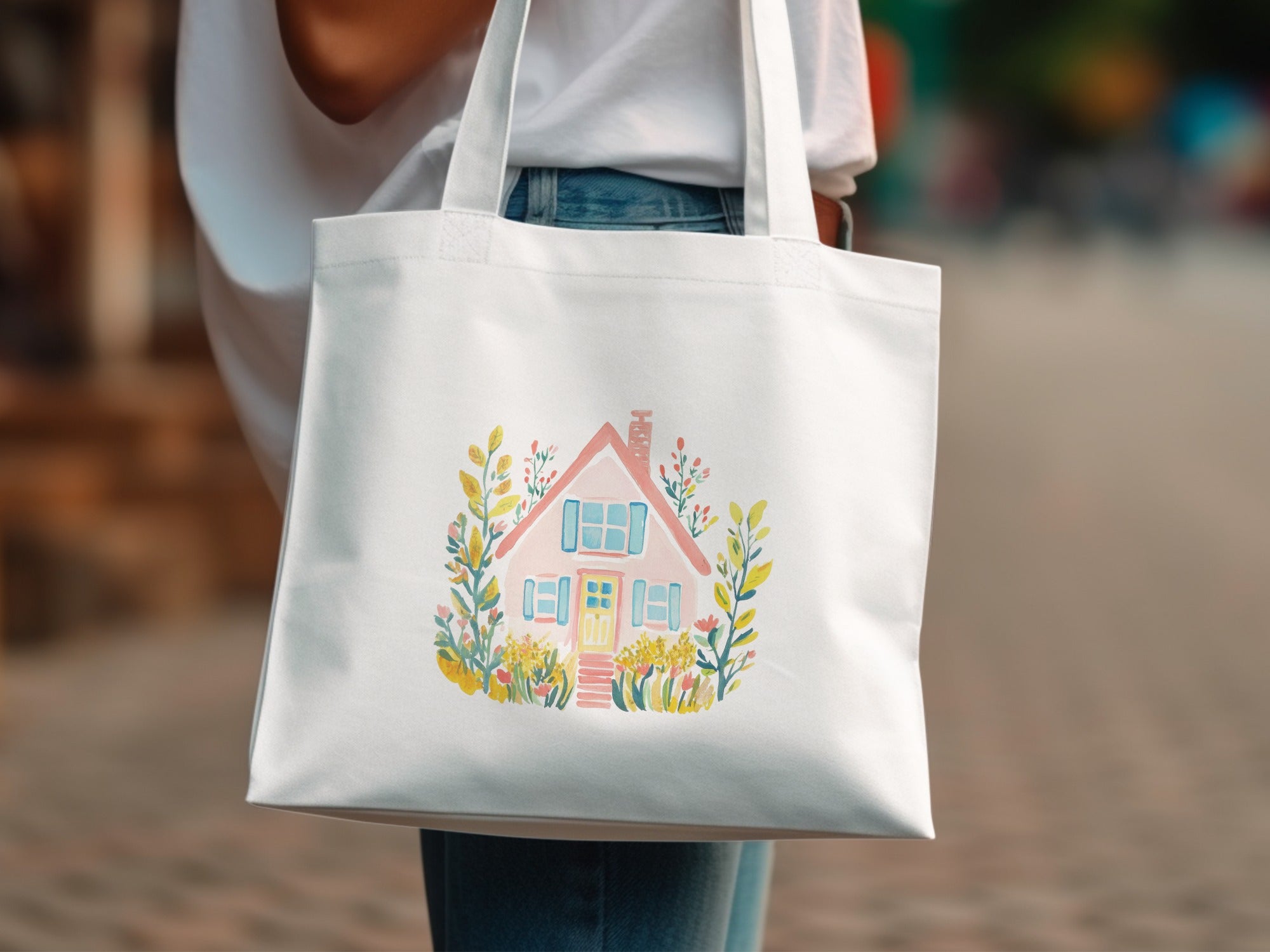 White tote bag with watercolor illustration of a cottage surrounded by flowers.