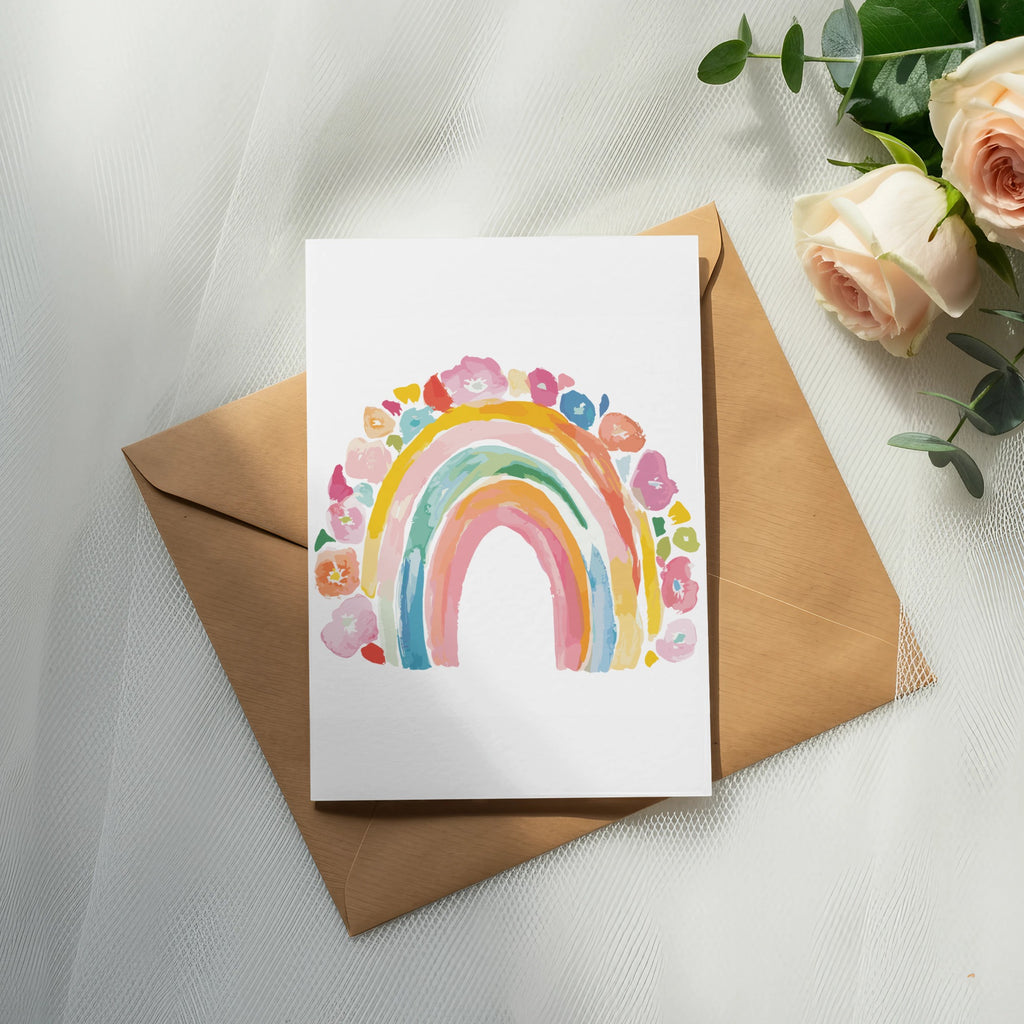 Watercolor rainbow art on a card atop a brown envelope, with roses and eucalyptus.