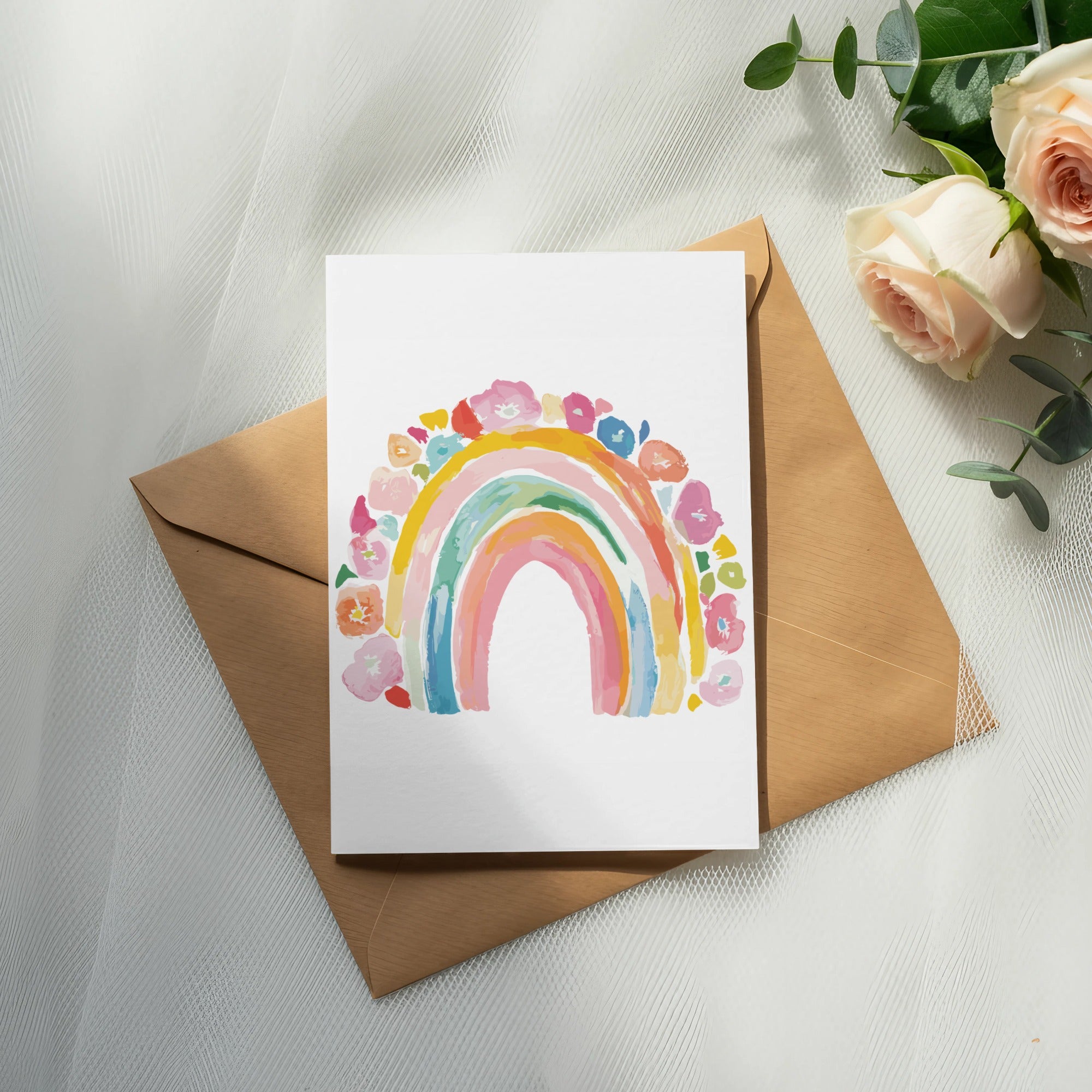 Watercolor rainbow art on a card atop a brown envelope, with roses and eucalyptus.