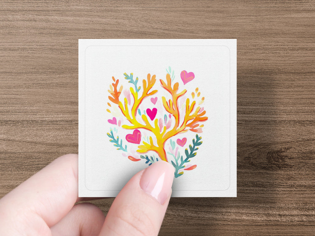 Hand holding a square card with a coral-like design and pink hearts.