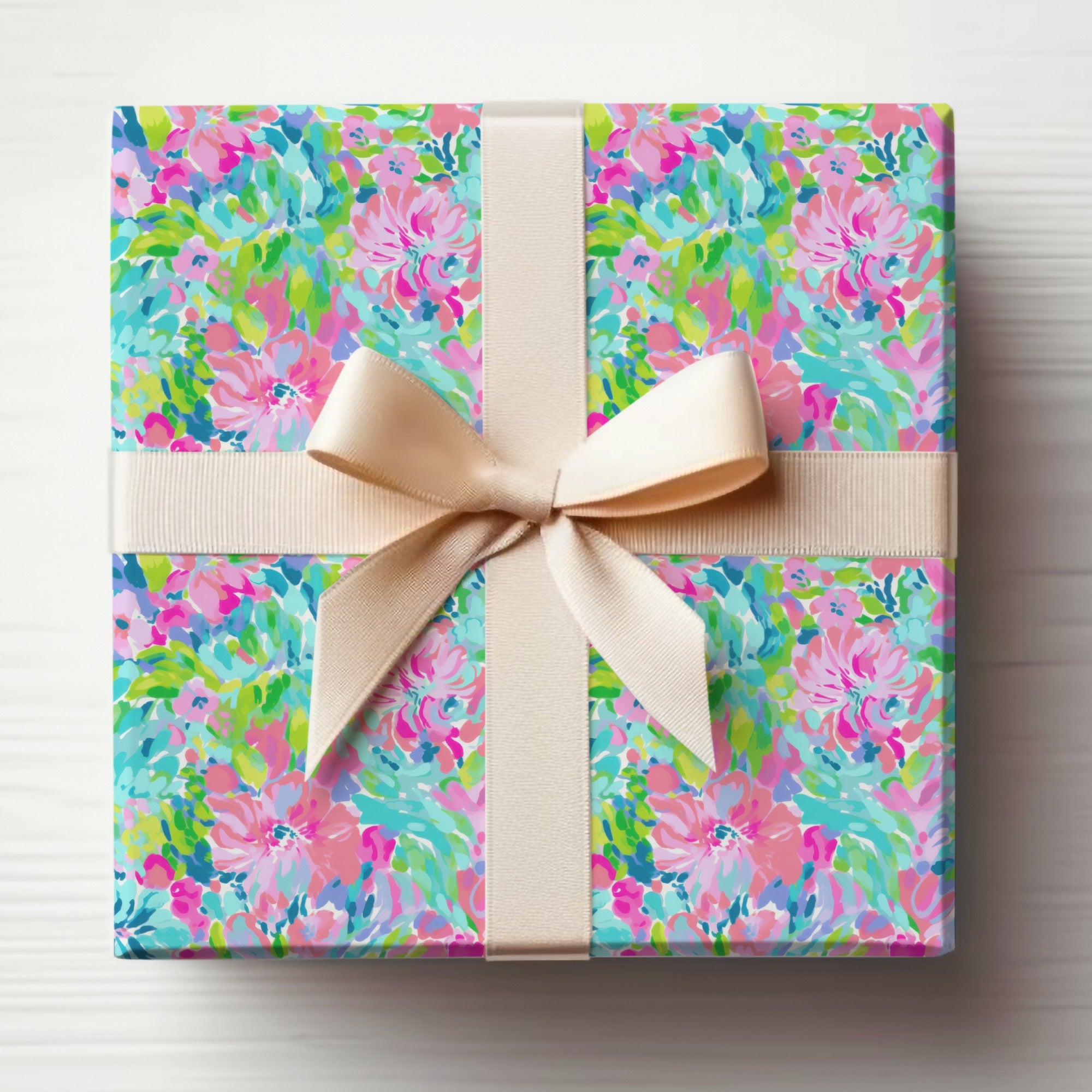 Colorful floral gift wrap with cream ribbon bow on a white surface.