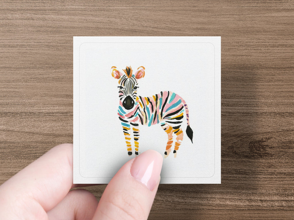 Colorful striped zebra illustration on a white card held by a hand.