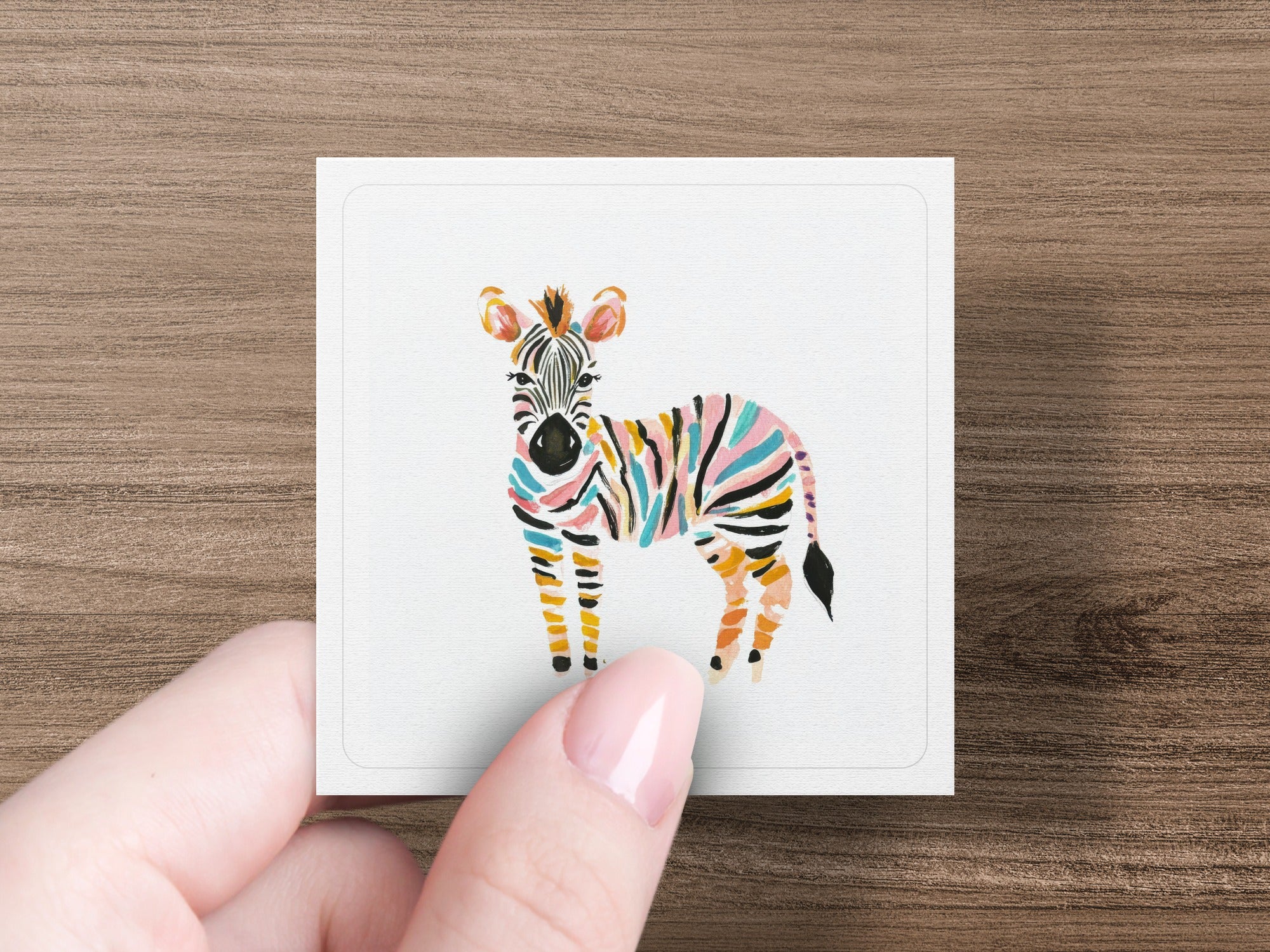 Colorful striped zebra illustration on a white card held by a hand.