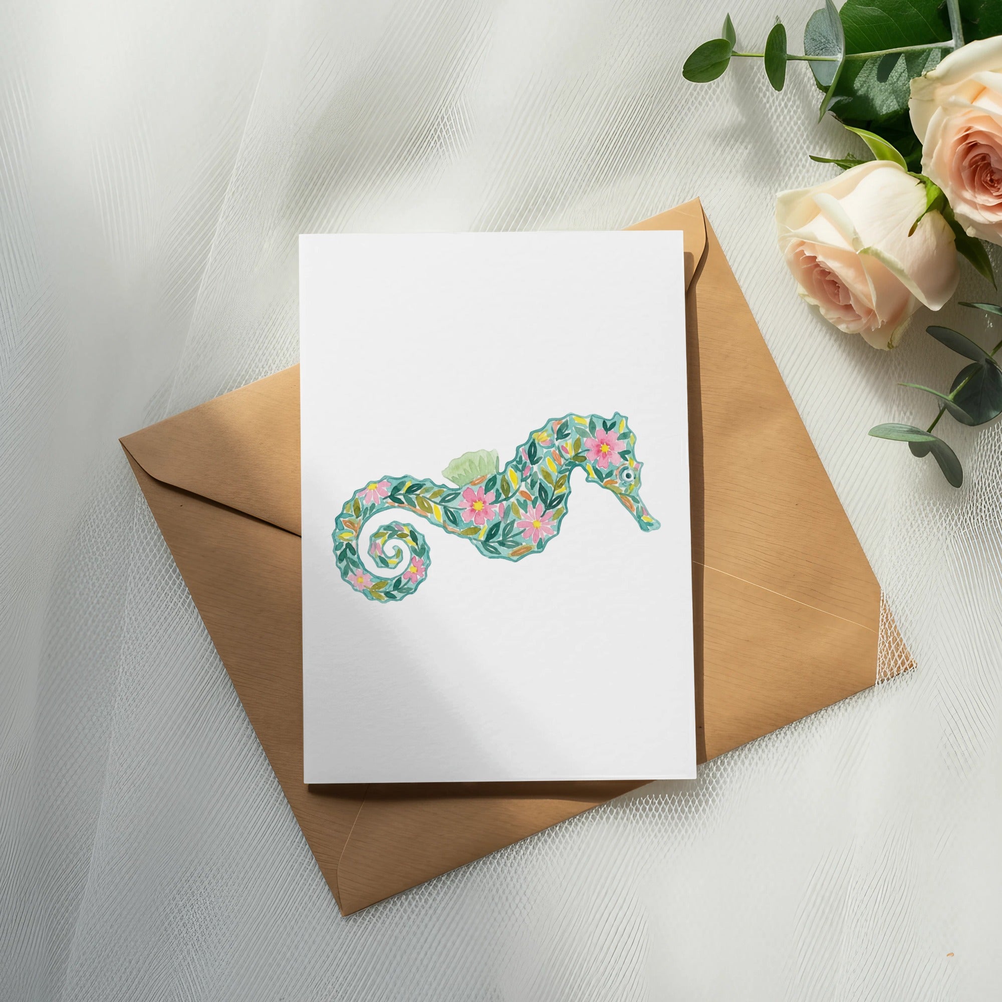 Watercolor seahorse illustration on card resting on brown envelope with roses.