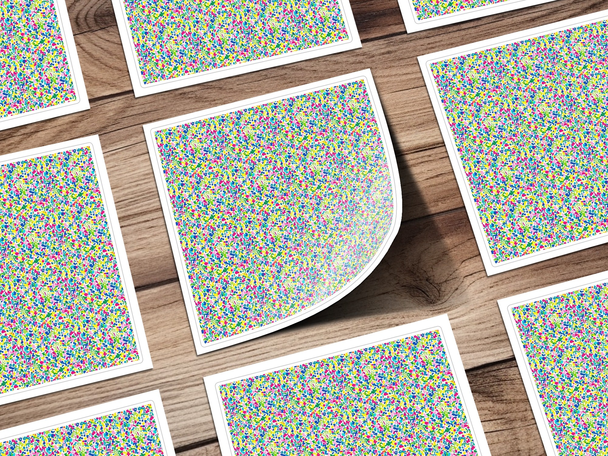 Pattern of colorful confetti on white squares arranged on a wooden surface.