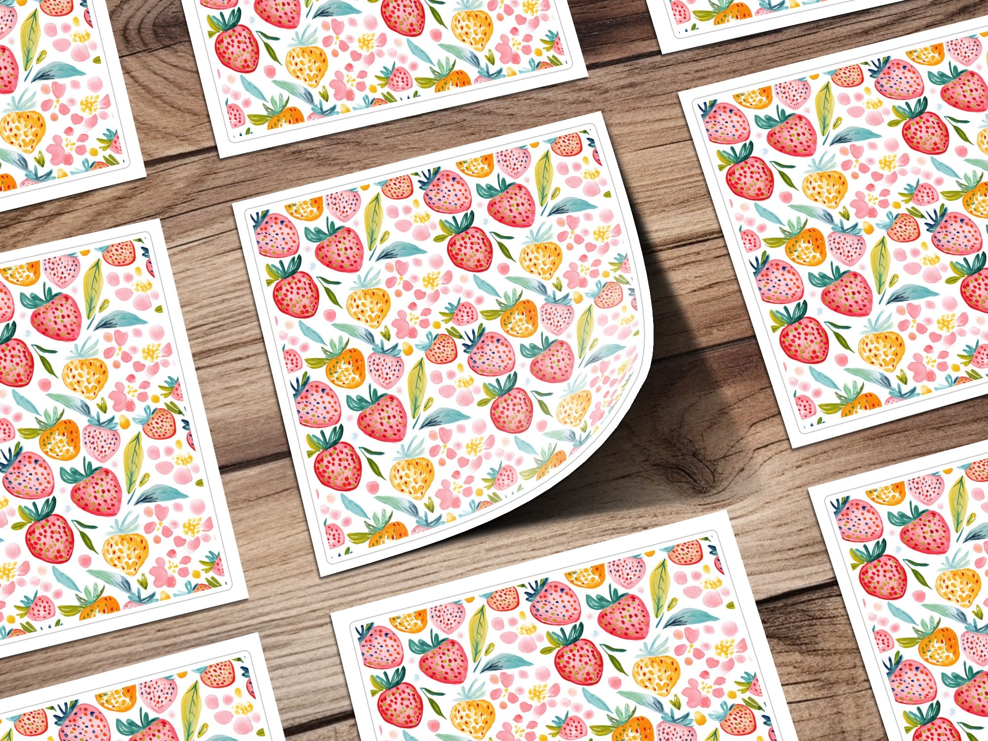 Watercolor strawberries and pink flowers pattern on cards, laid out on wood.