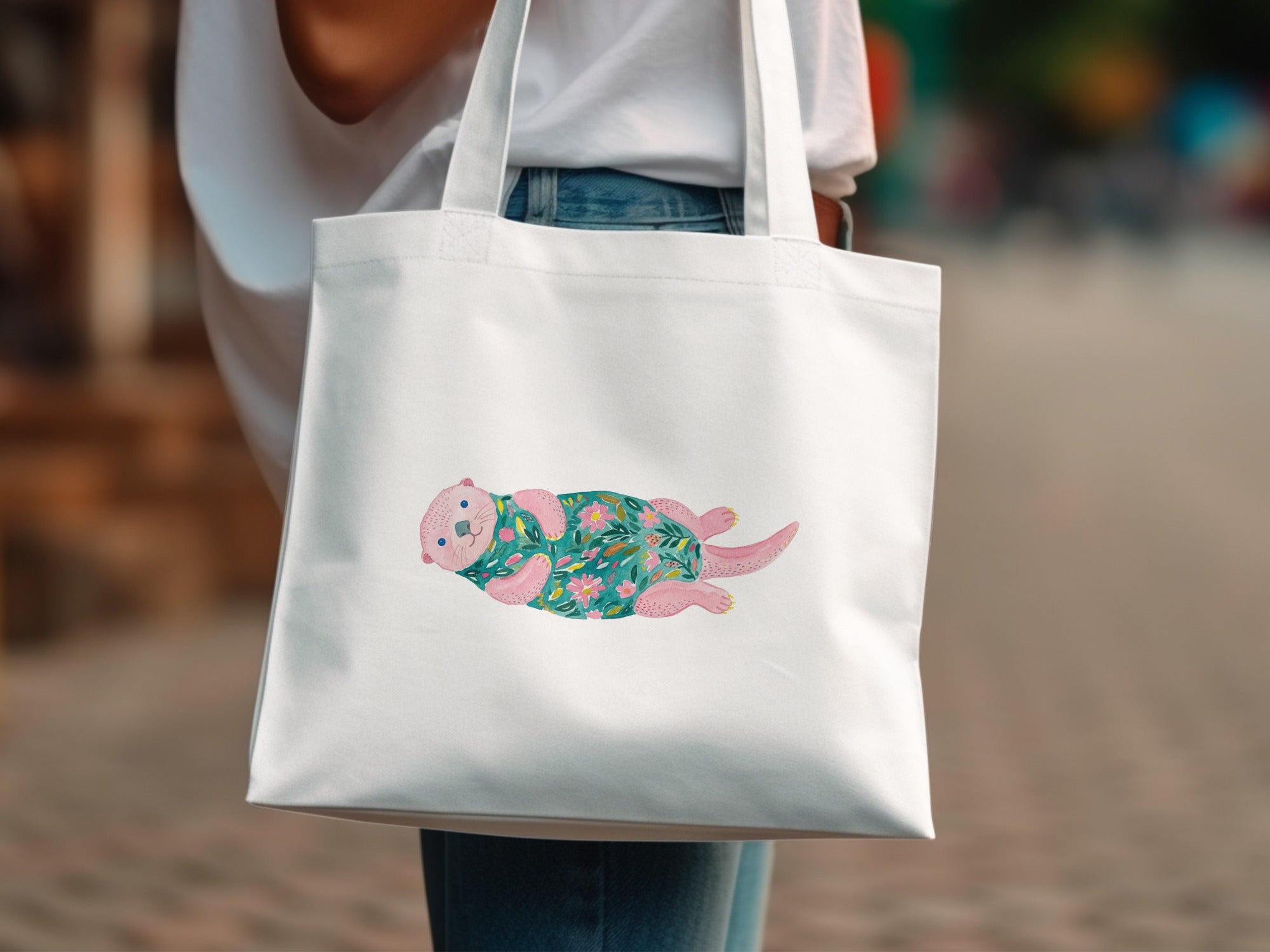 White canvas tote bag with a pink otter illustration on a floral background.