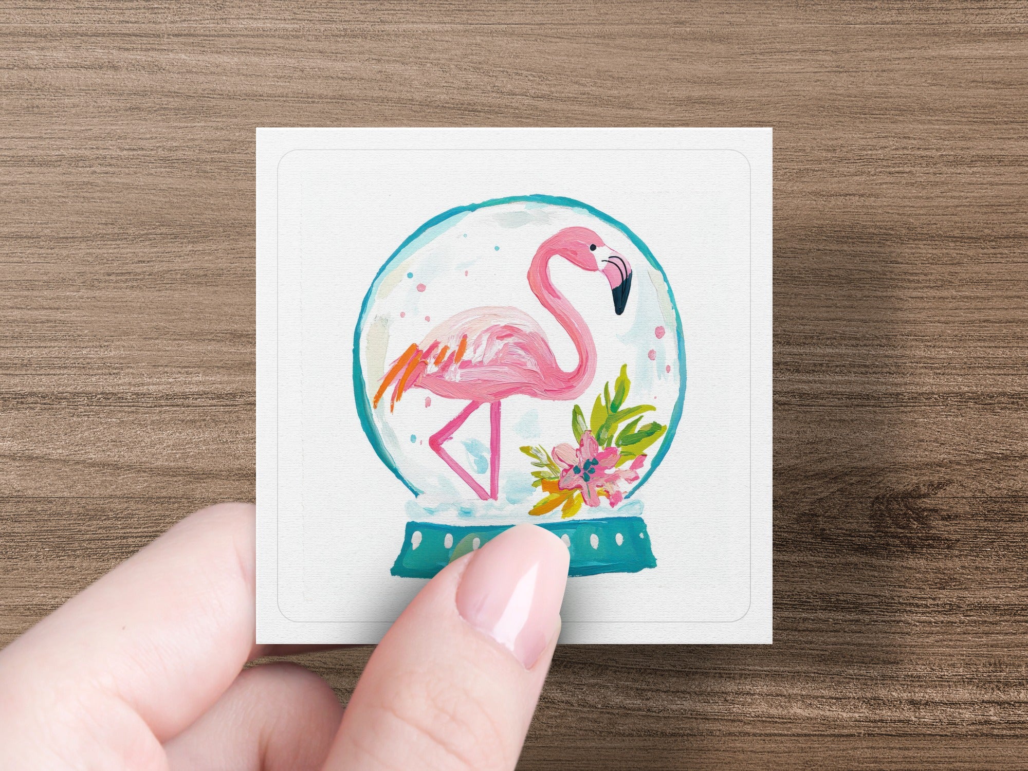 Flamingo inside a snow globe with flowers, held by a hand.