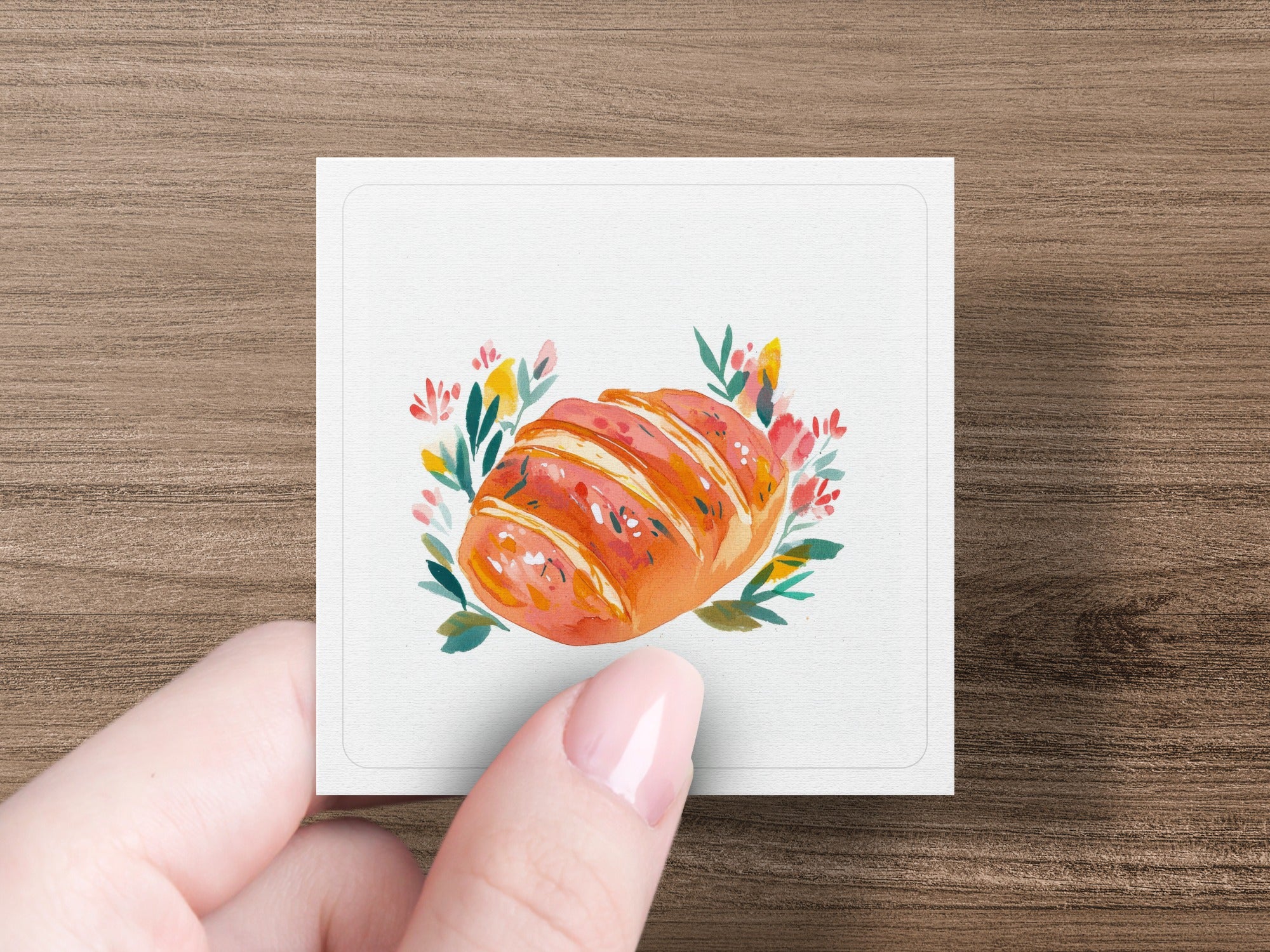 Crusty loaf of bread with floral accents on a white card held by a hand.