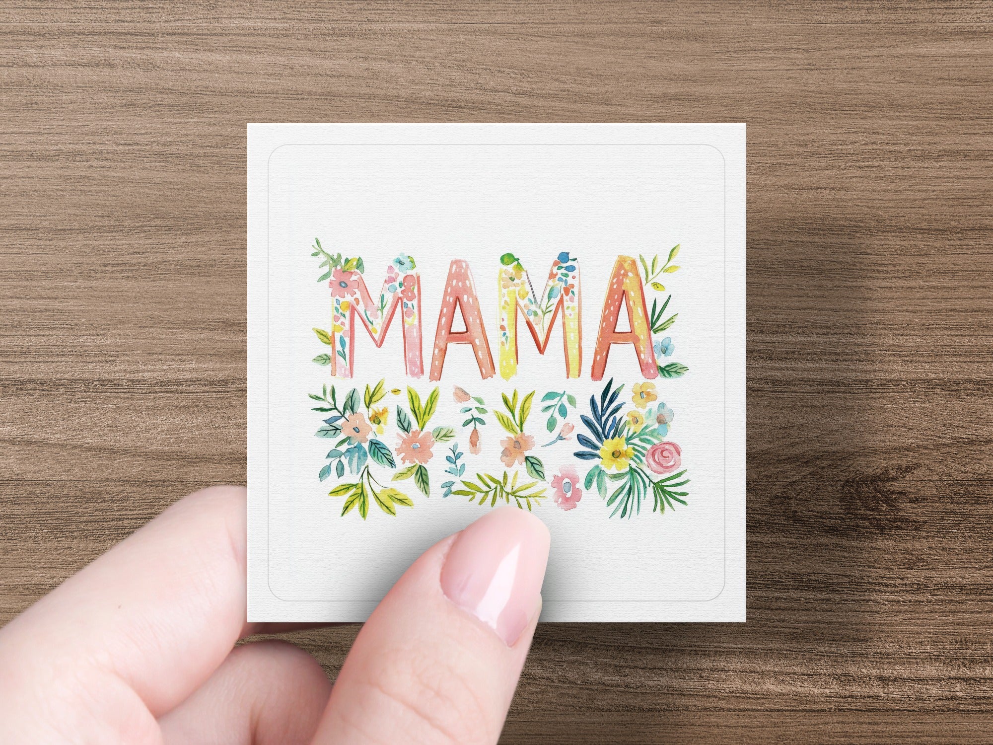 Floral "MAMA" lettering on a card held by a hand.