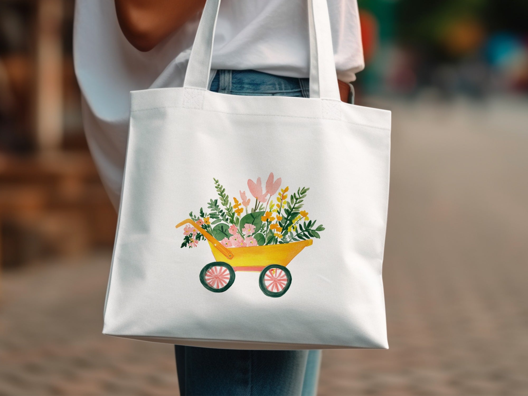 White tote bag with watercolor illustration of a yellow wheelbarrow full of flowers.