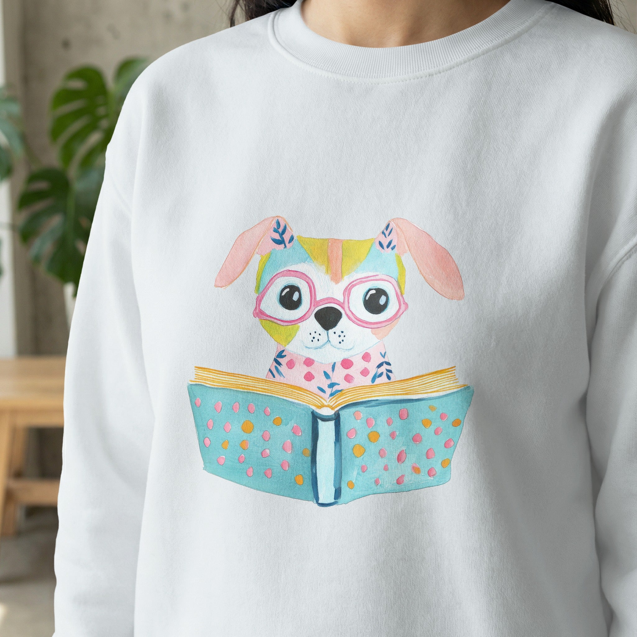 White sweatshirt with watercolor illustration of a dog wearing glasses reading a book.