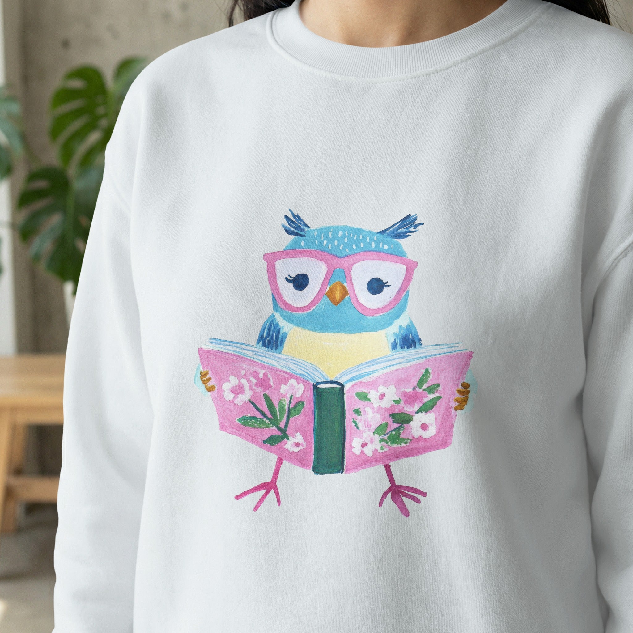 White sweatshirt with a cartoon owl wearing pink glasses reading a book.