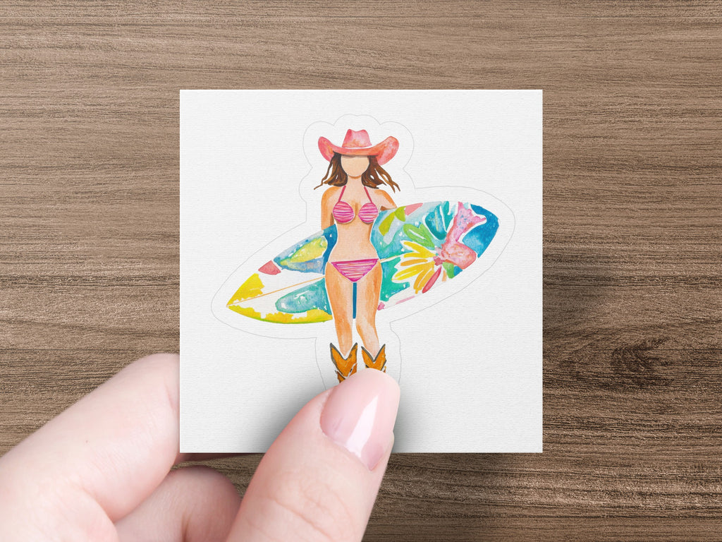 Woman in cowboy hat and bikini holds a surfboard, standing in cowboy boots.