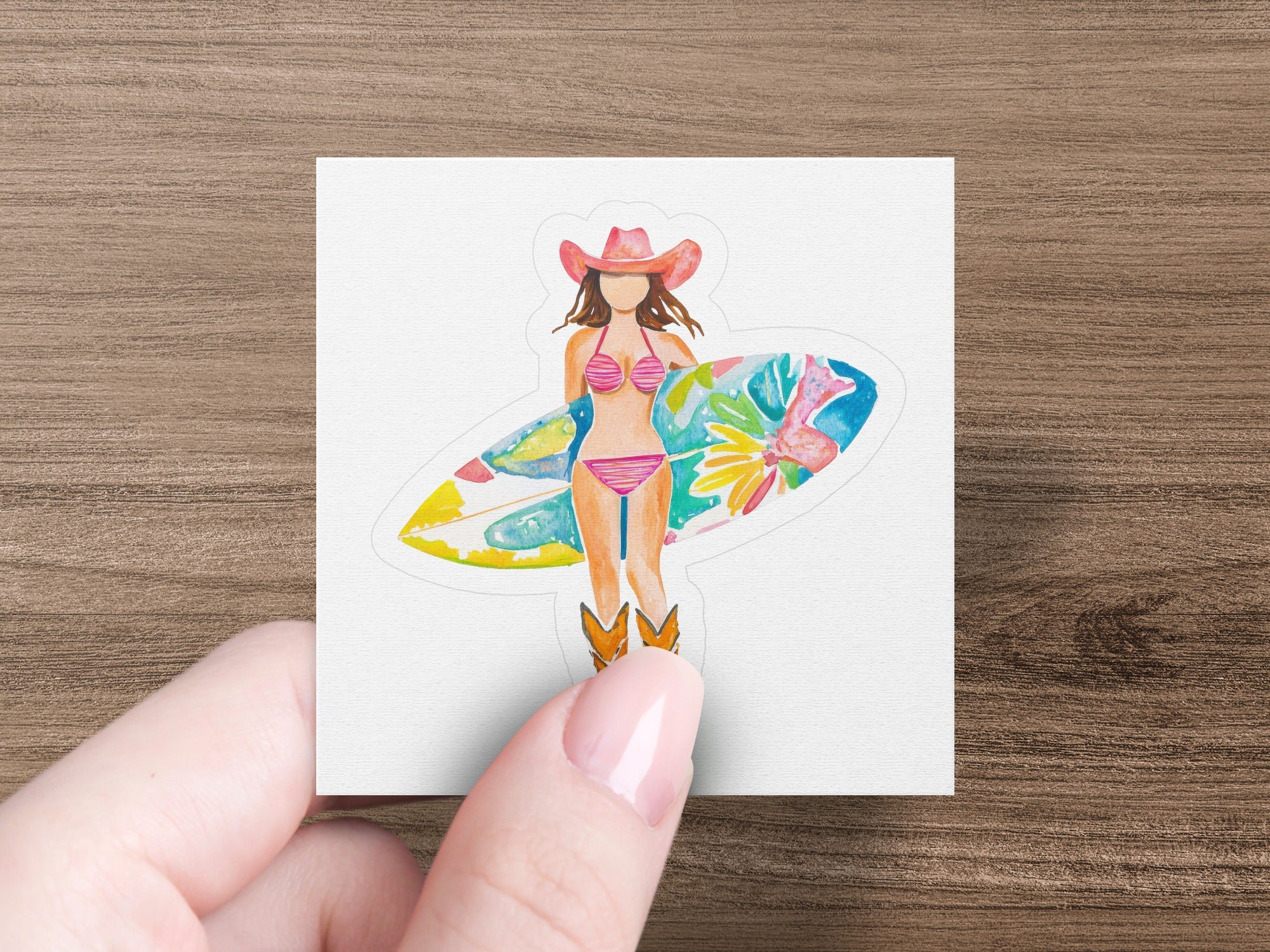 Woman in cowboy hat and bikini holds a surfboard, standing in cowboy boots.