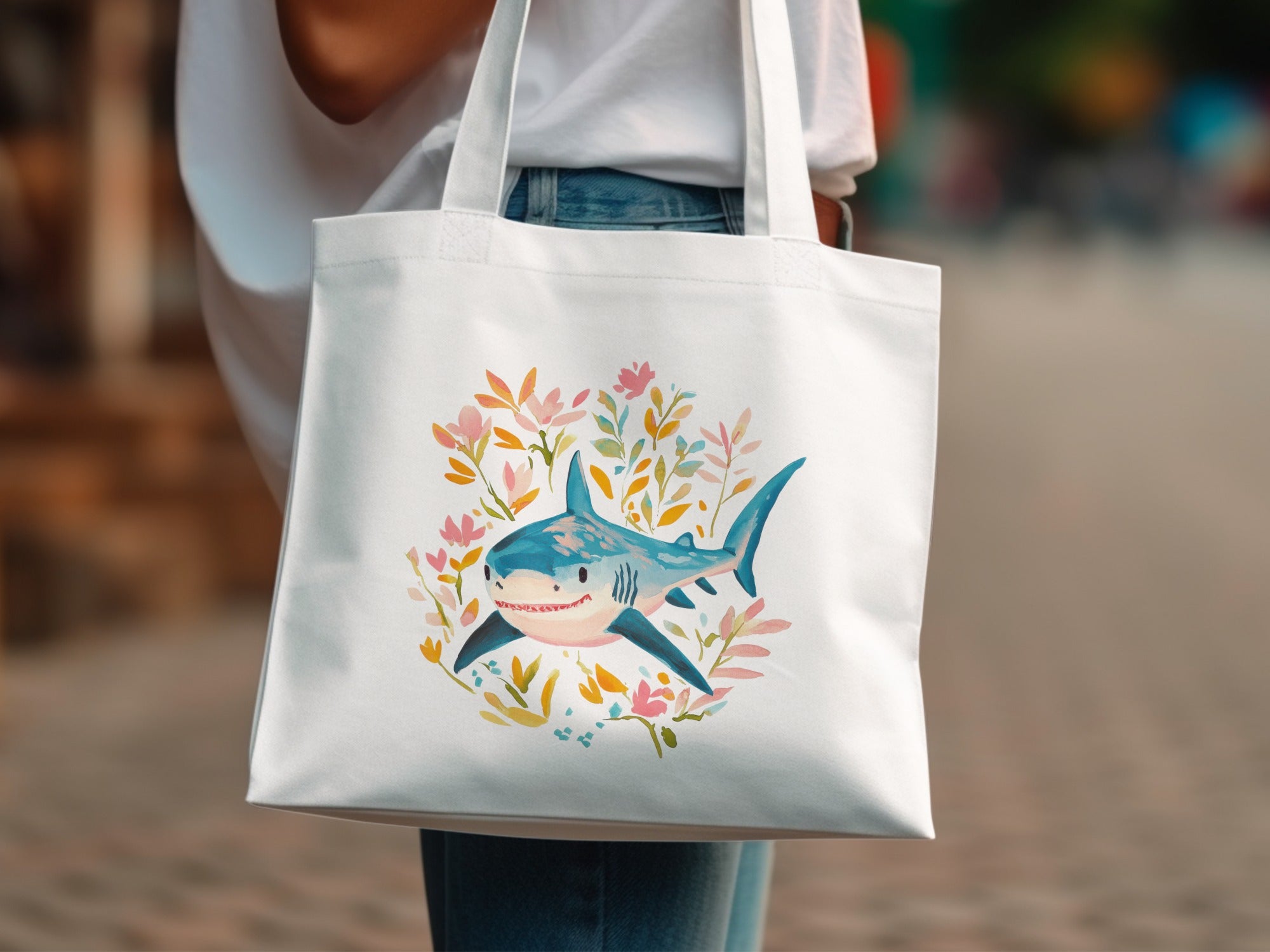 White canvas tote bag with a smiling shark surrounded by floral watercolor accents.