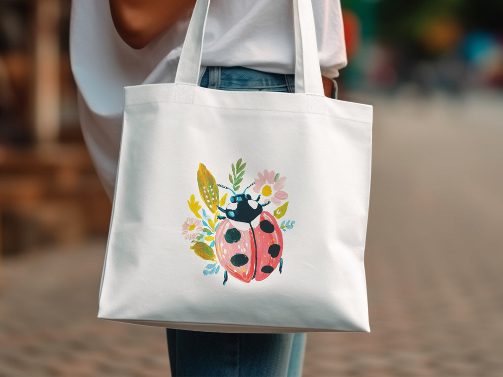 White tote bag with ladybug and floral illustration.