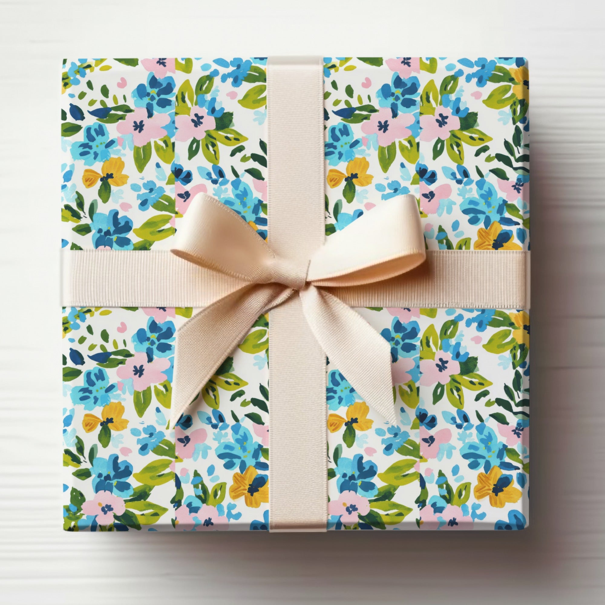 Gift-wrapped box with blue, pink, and yellow floral pattern and beige ribbon.